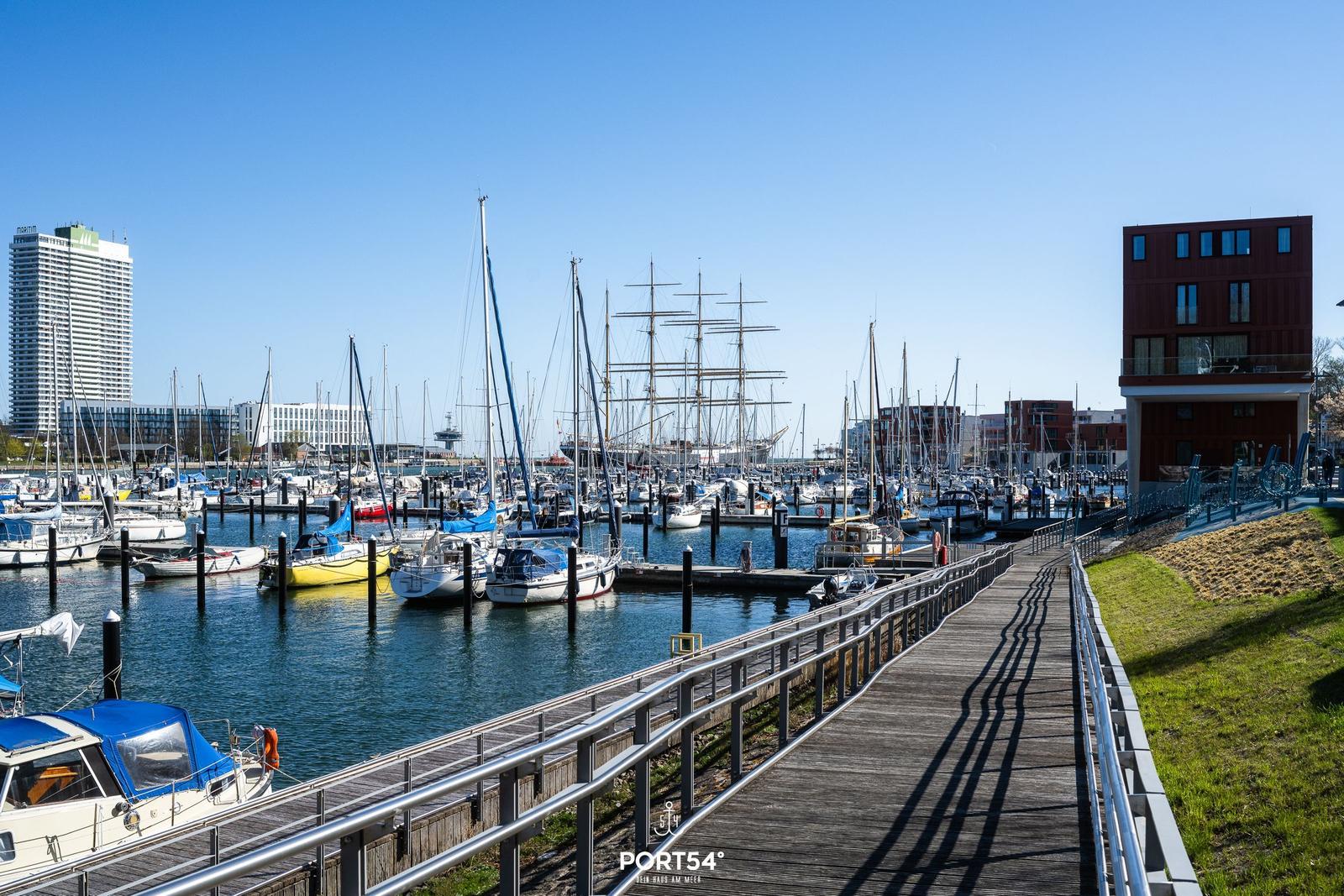 Holzpromenade am Hafen mit Booten und modernen Gebäuden im Hintergrund.