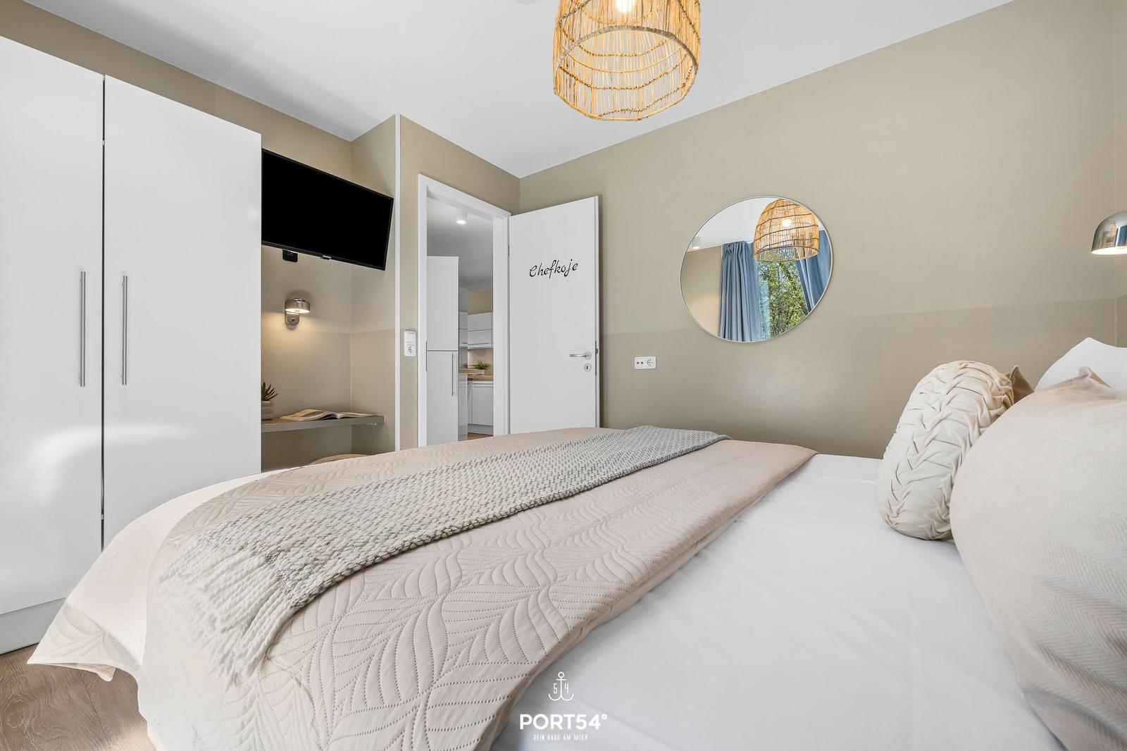 Schlafzimmer mit Bett, Kleiderschrank und Spiegel an der Wand.