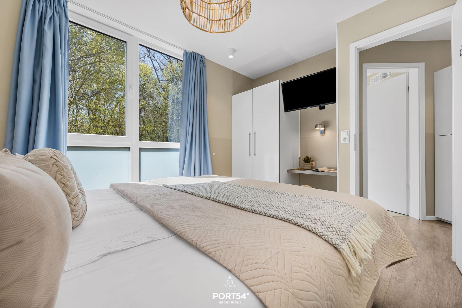 Schlafzimmer mit Bett, Fenster und Gardinen. TV und Schrank sind sichtbar.