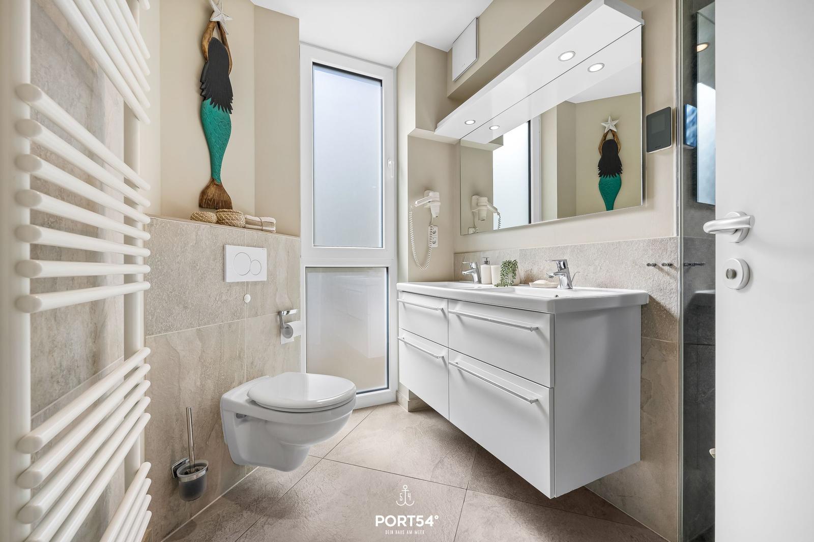Badezimmer mit Waschbecken, Spiegel, Toilette und Dusche. Wandheizung und Meerjungfrau-Dekoration.