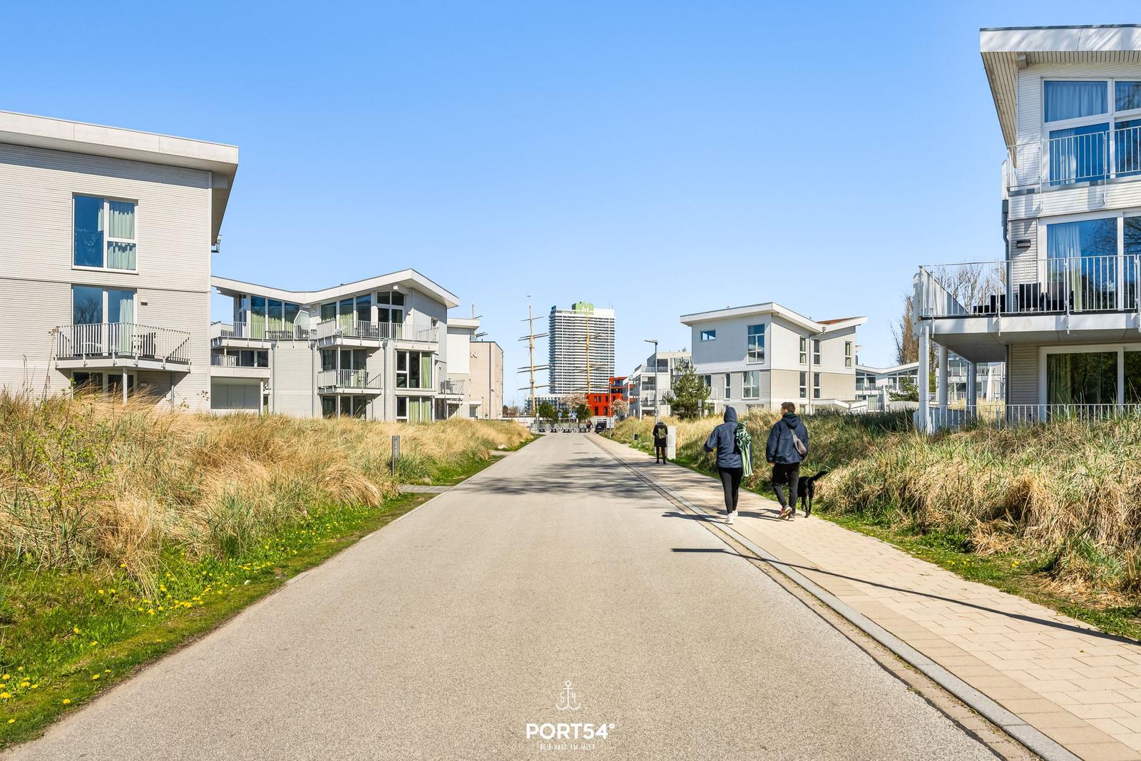 Wohngebiet mit modernen Häusern und Promenade. Menschen spazieren mit Hund.