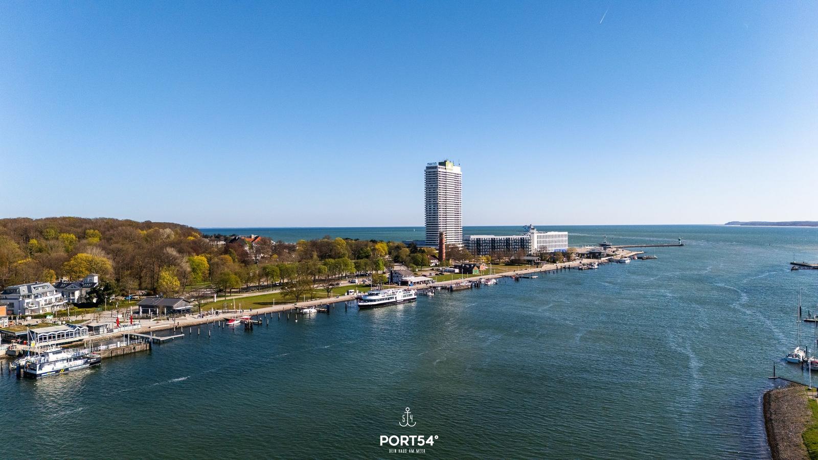 Hafen mit Booten, Strandpromenade und Hochhaus am Meer.