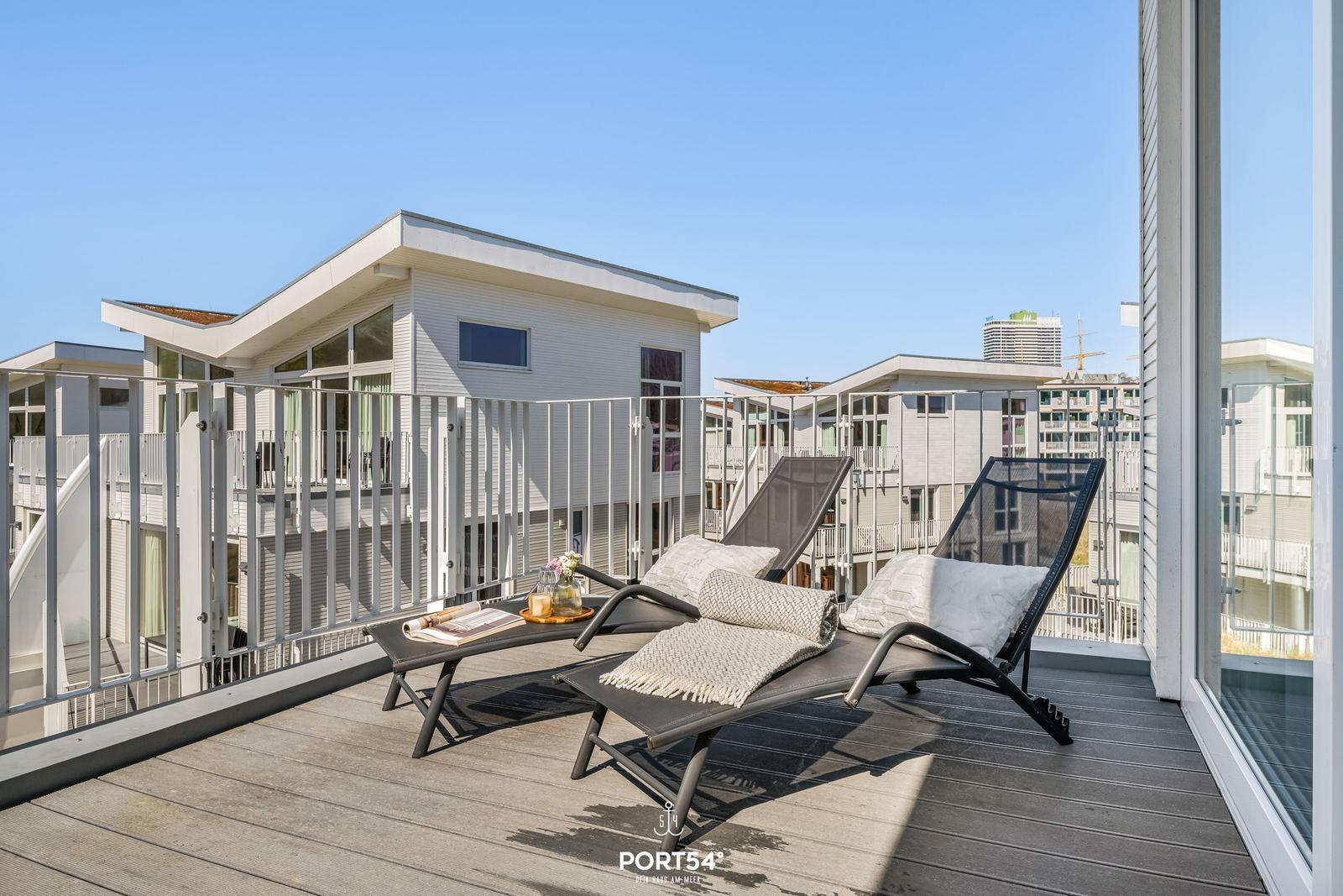 Terrasse mit zwei Liegestühlen und Blick auf moderne Gebäude.