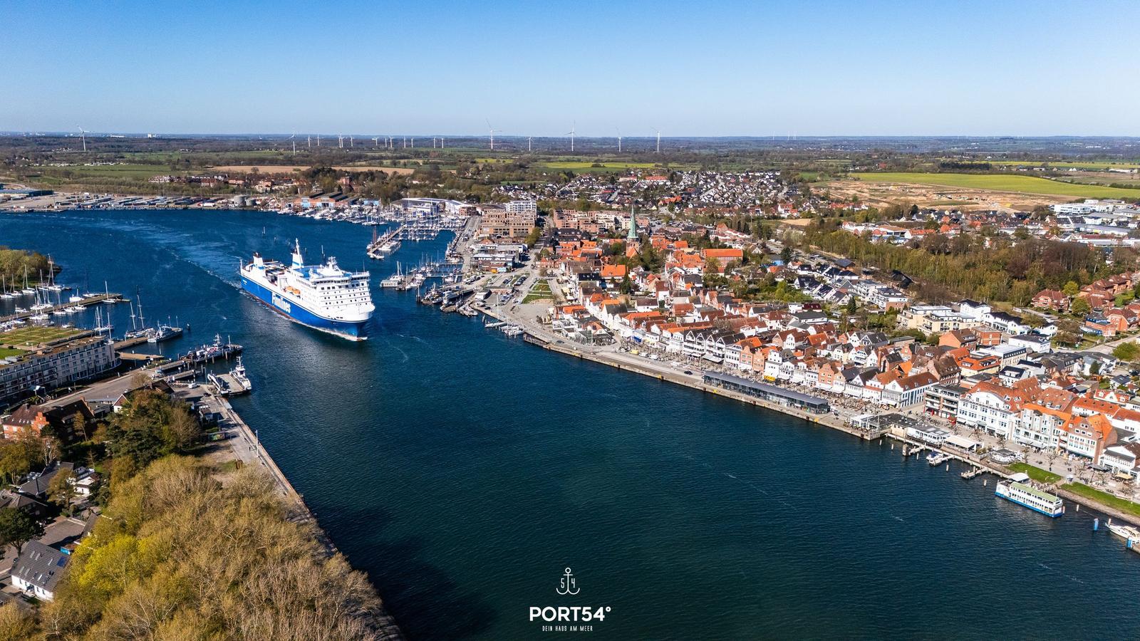 Hafenstadt mit Fährschiff und Booten. Blick auf Häuser und Windkraftanlagen.
