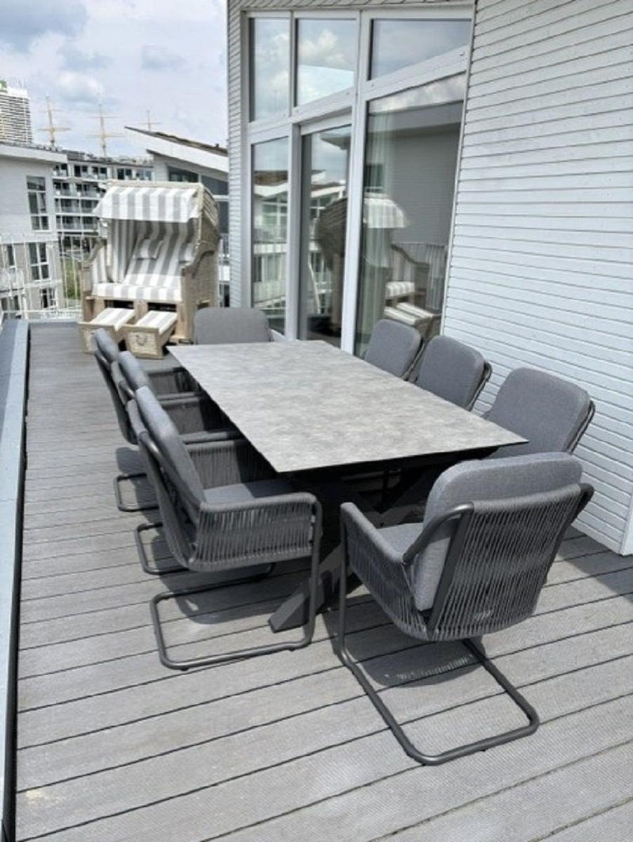 Terrasse mit großer Tisch und acht Stühlen, daneben Strandkorb und Glasfassade.