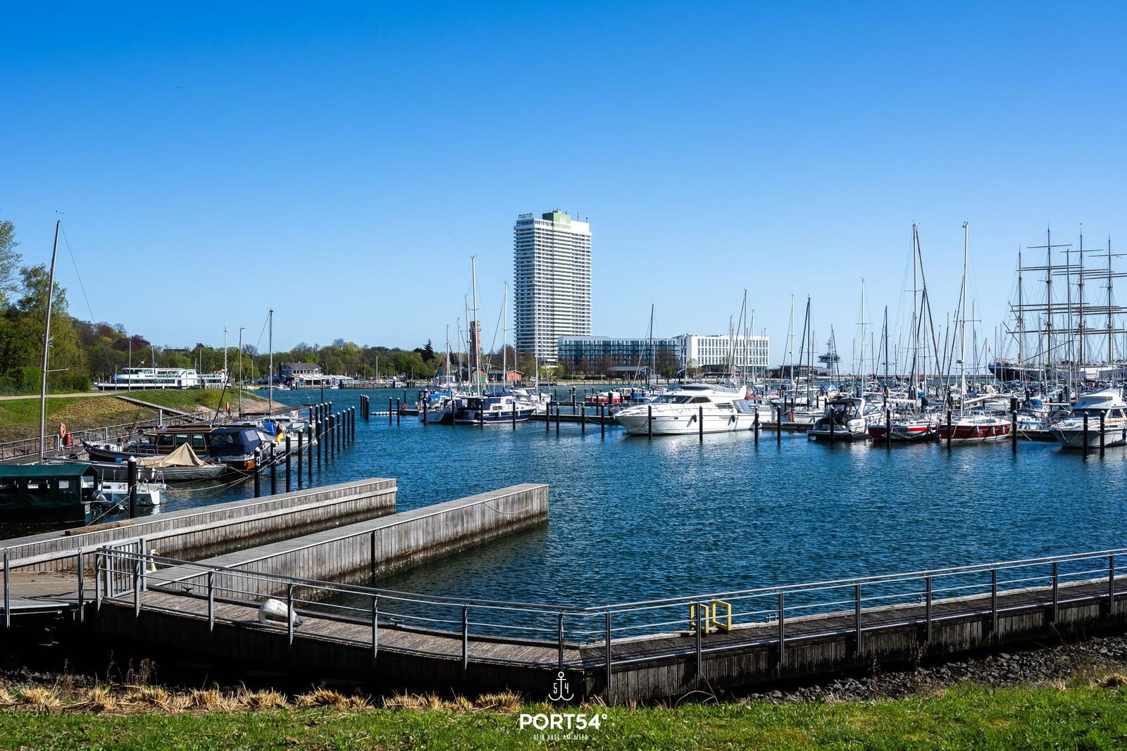 Hafen mit Booten und modernen Gebäuden im Hintergrund.