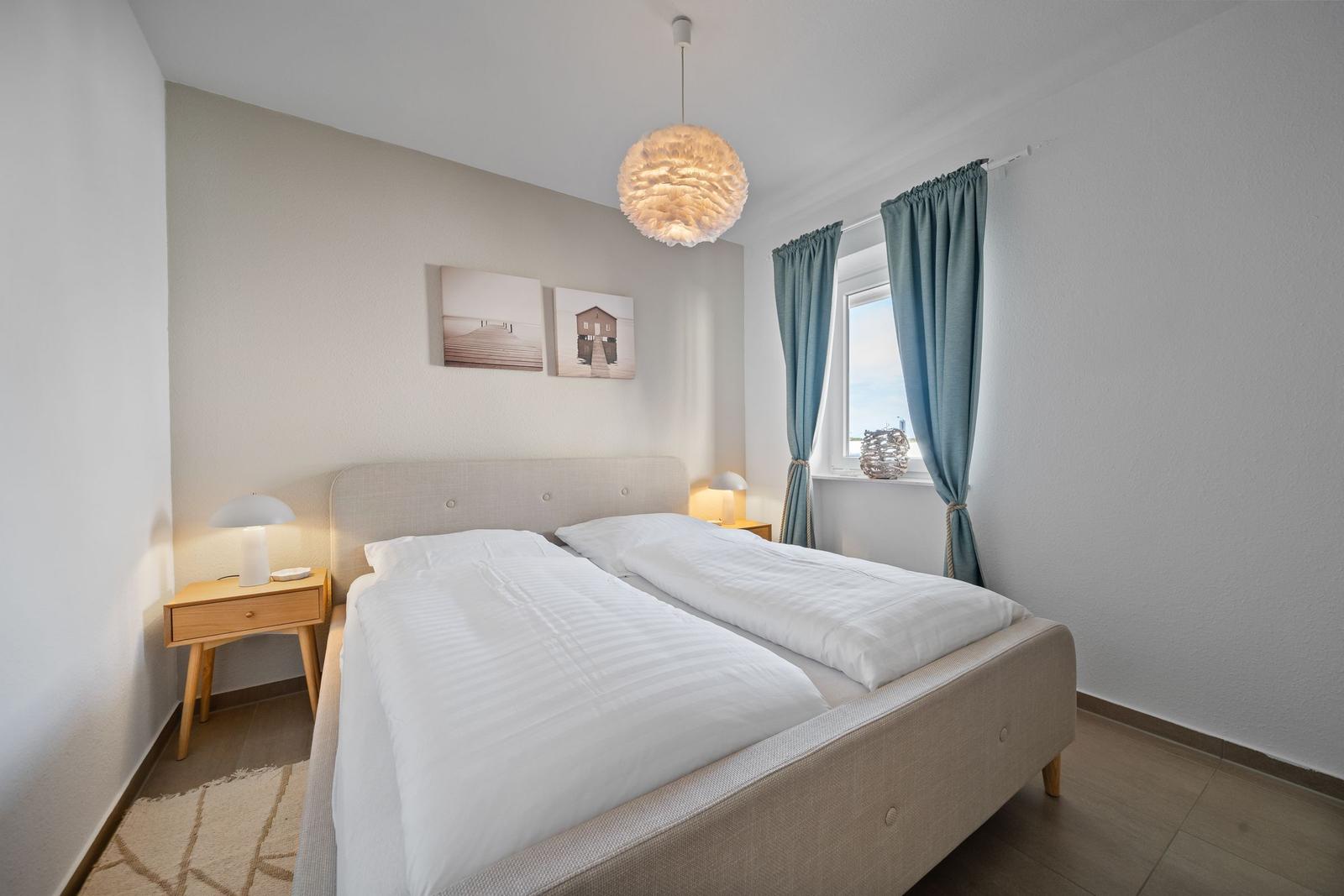 Schlafzimmer mit Doppelbett, Nachttischen und Fenster mit Vorhängen.