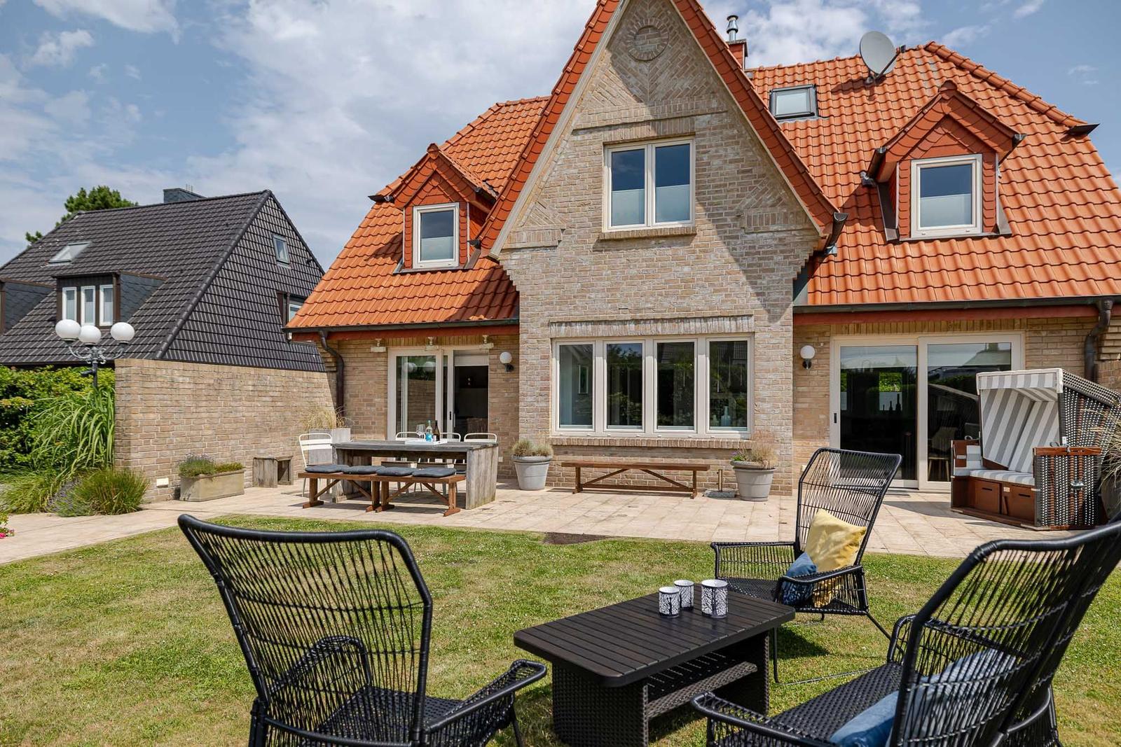 Haus mit Terrasse und Gartenbereich mit Sitzmöbeln und Tisch.