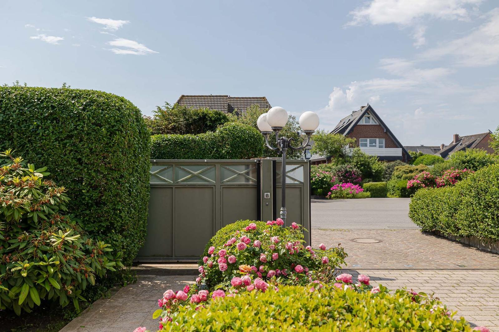 Eingangstor mit Rosenbeete und gepflegtem Garten. Hinterhof mit Sicht auf Wohnhäuser.