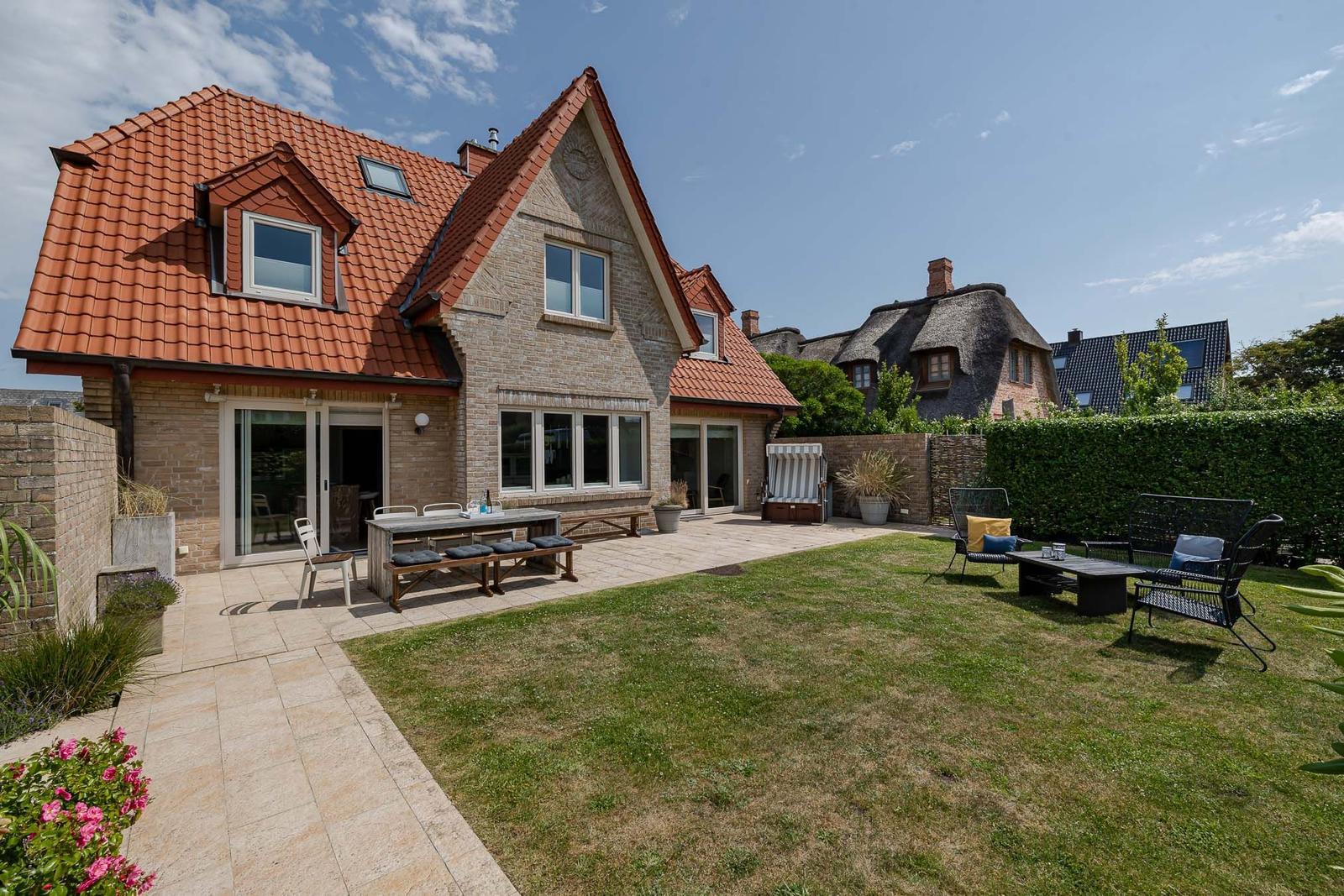 Haus mit Terrasse, Garten und Außensitzgelegenheiten unter blauem Himmel.