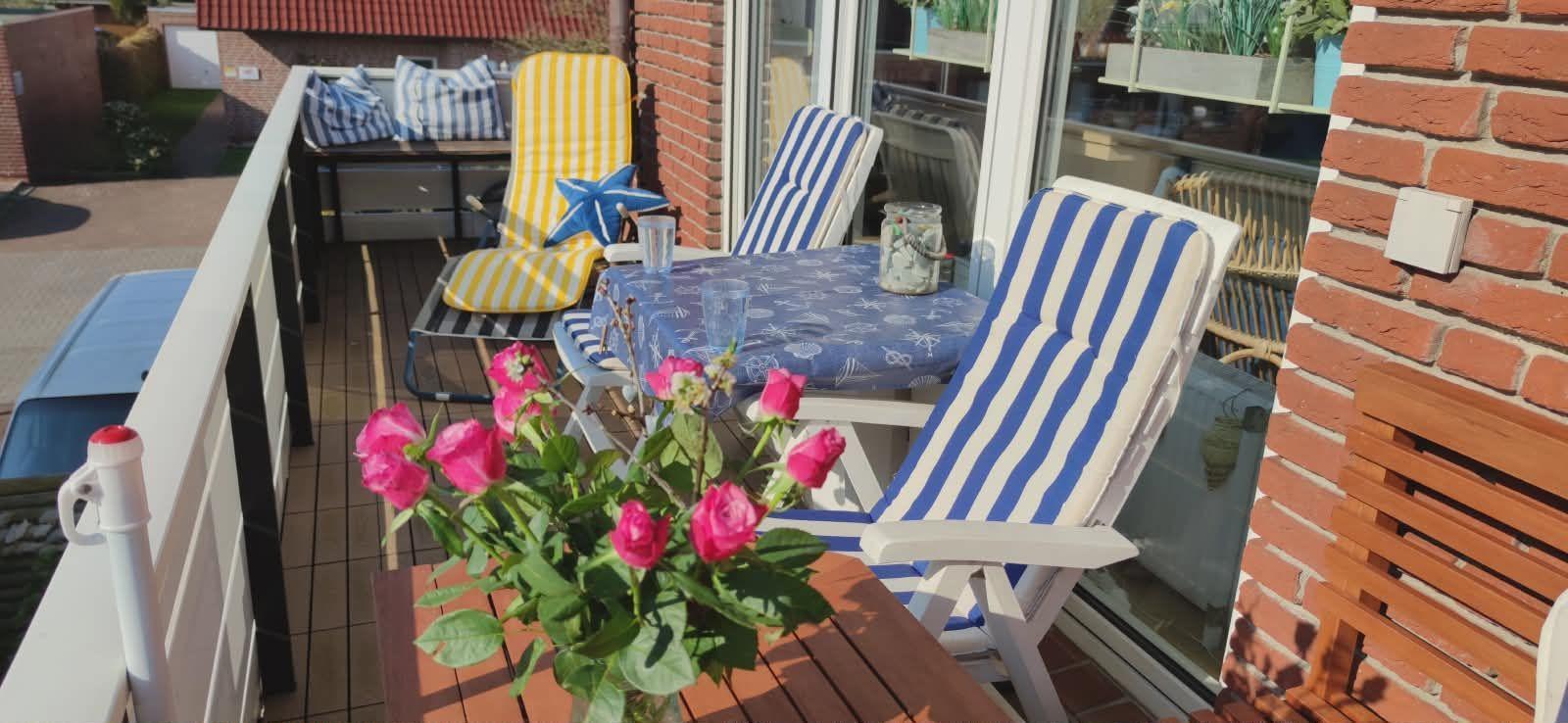 Terrasse mit Stühlen, Tisch und Blumen. Blick auf Haus und Straße.