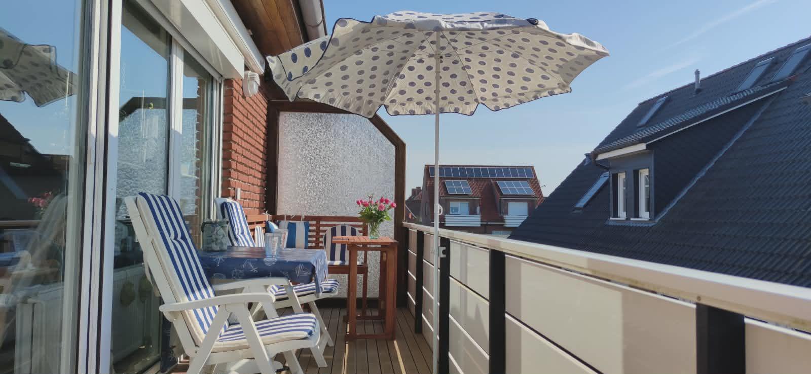 Terrasse mit Sonnenschirm, Tisch und Stühlen. Blick auf Dächer und Solaranlagen.
