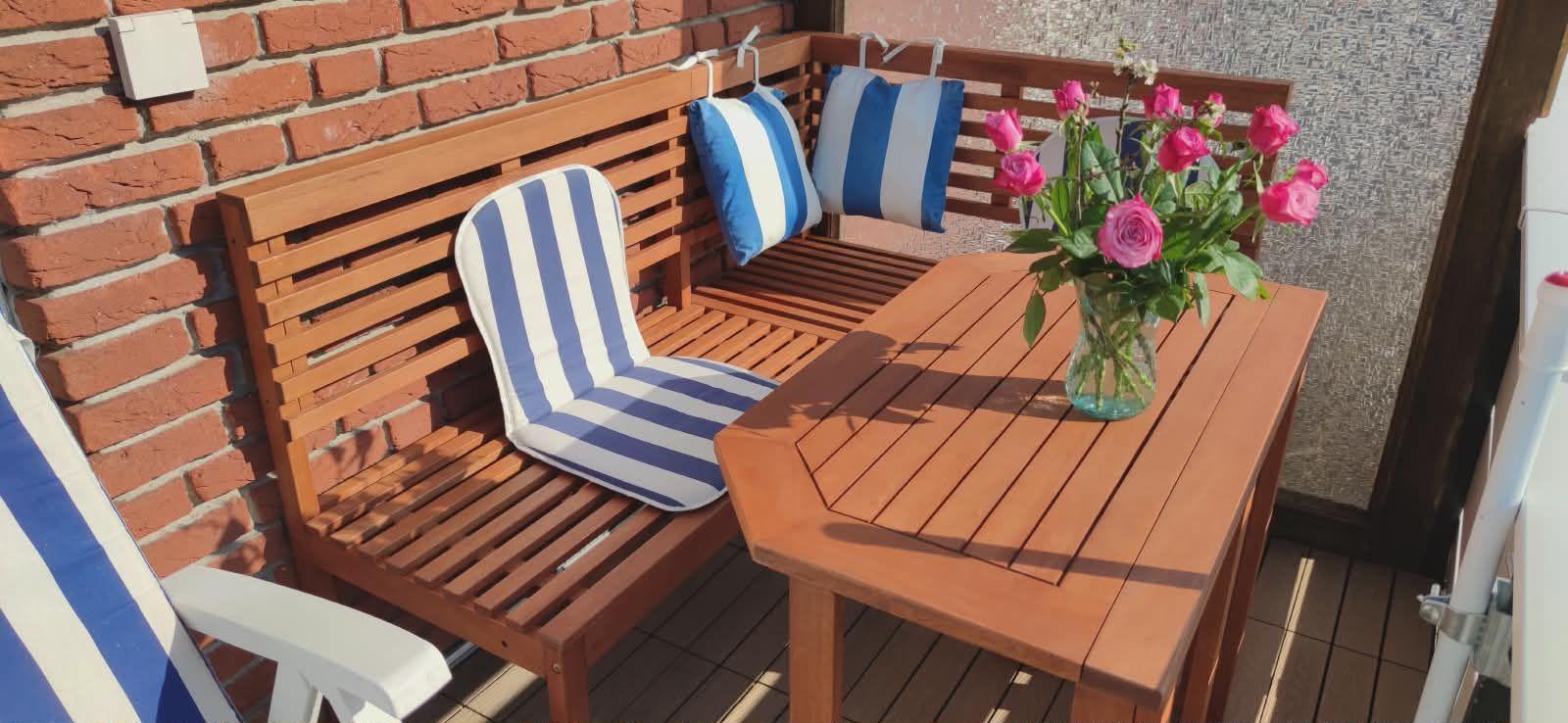 Terrasse mit Holztisch, Stühlen und Blumenstrauß in Glasvase.