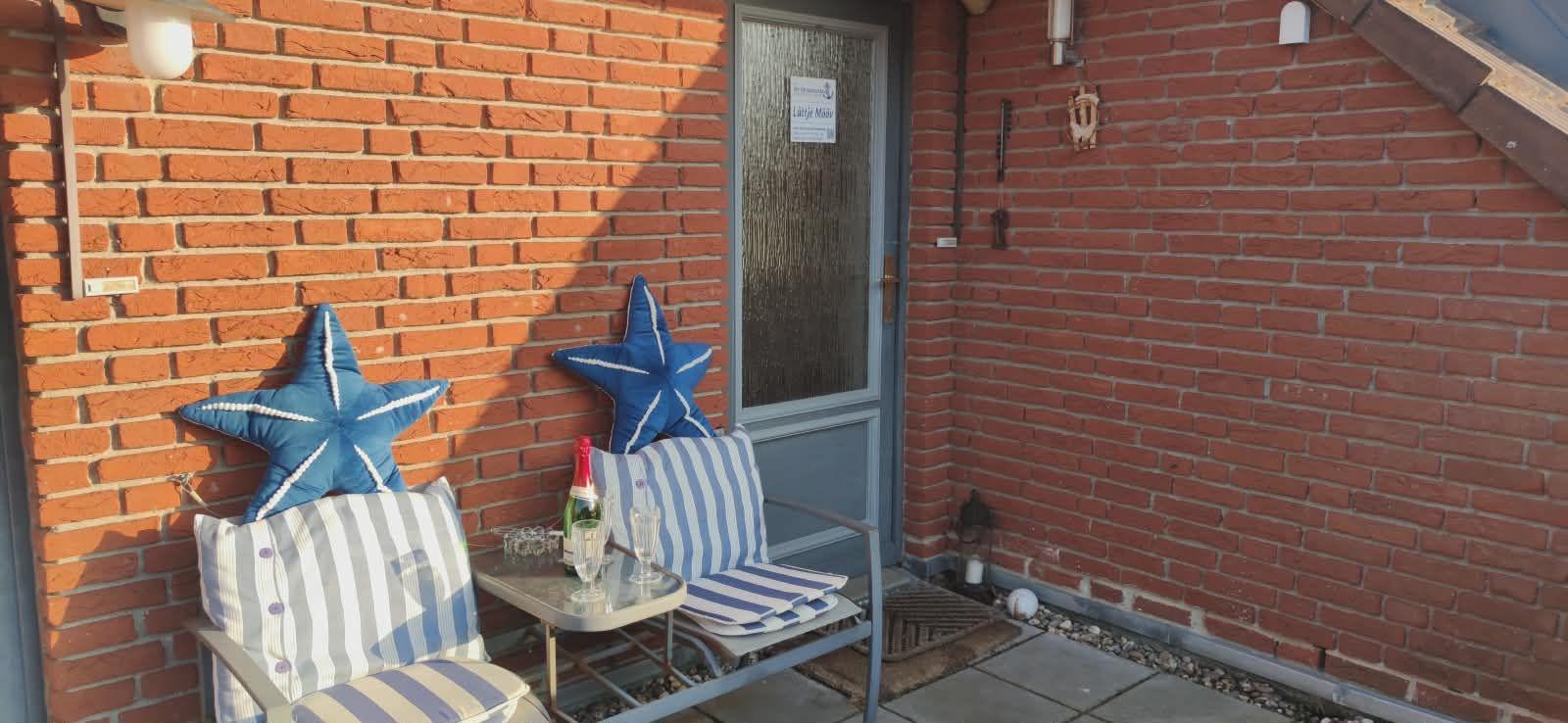 Terrasse mit zwei Stühlen, Tisch und blauen Sternkissen vor rotem Backsteinhaus.