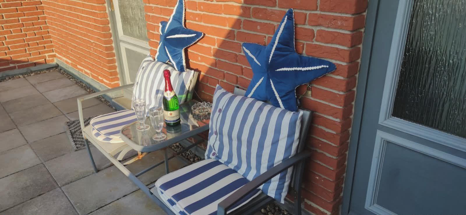 Terrasse mit Stuhl, Tisch und blauen Sternkissen an Backsteinwand