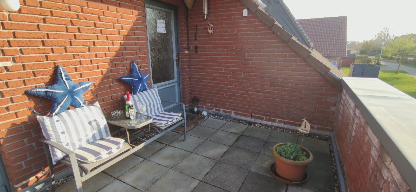 Terrasse mit Sitzgelegenheit, Pflanze und Sternkissen an Backsteinwand