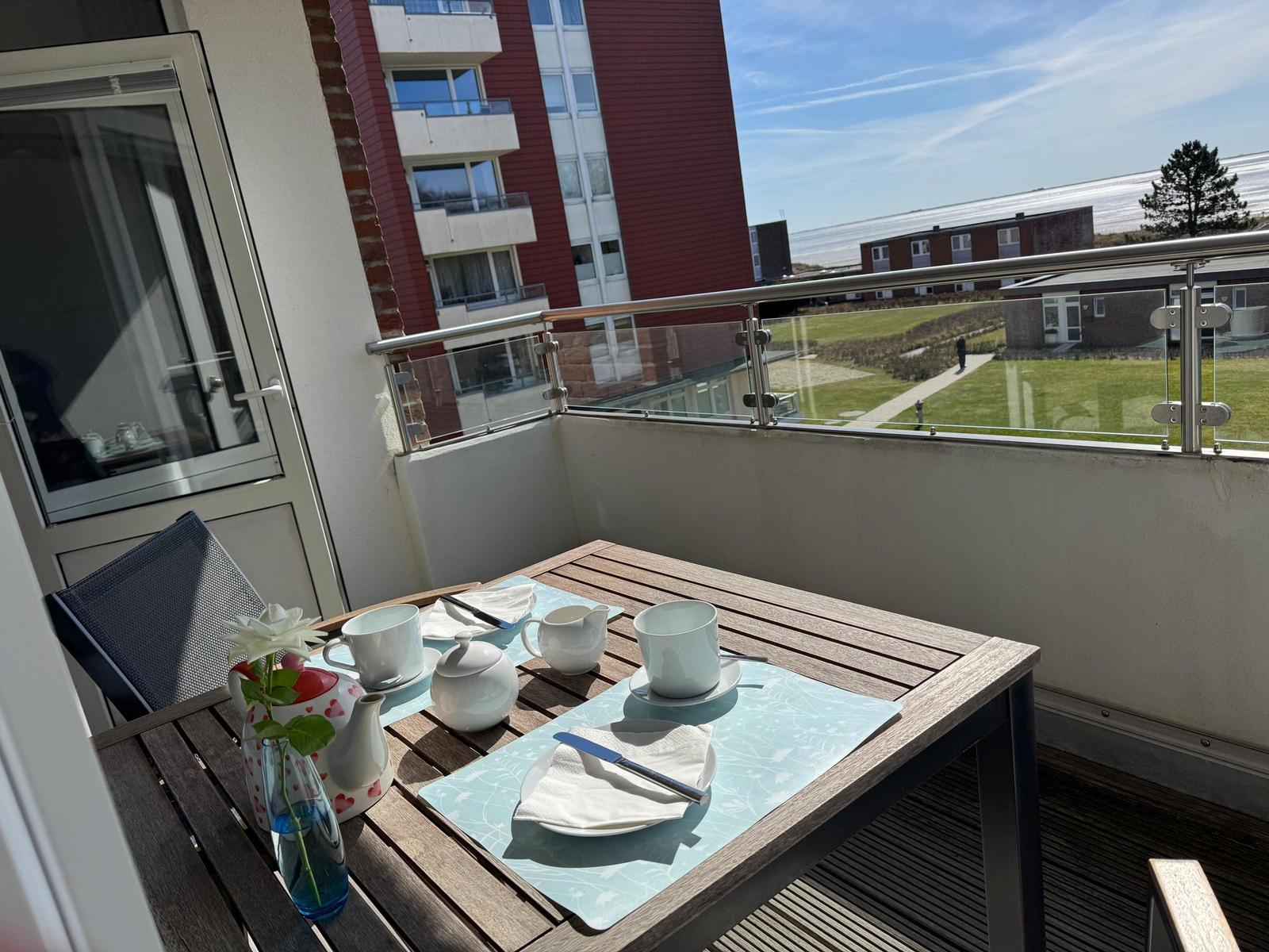Terrasse mit Tisch, Stühlen und Blick auf Grünfläche und Gebäude.