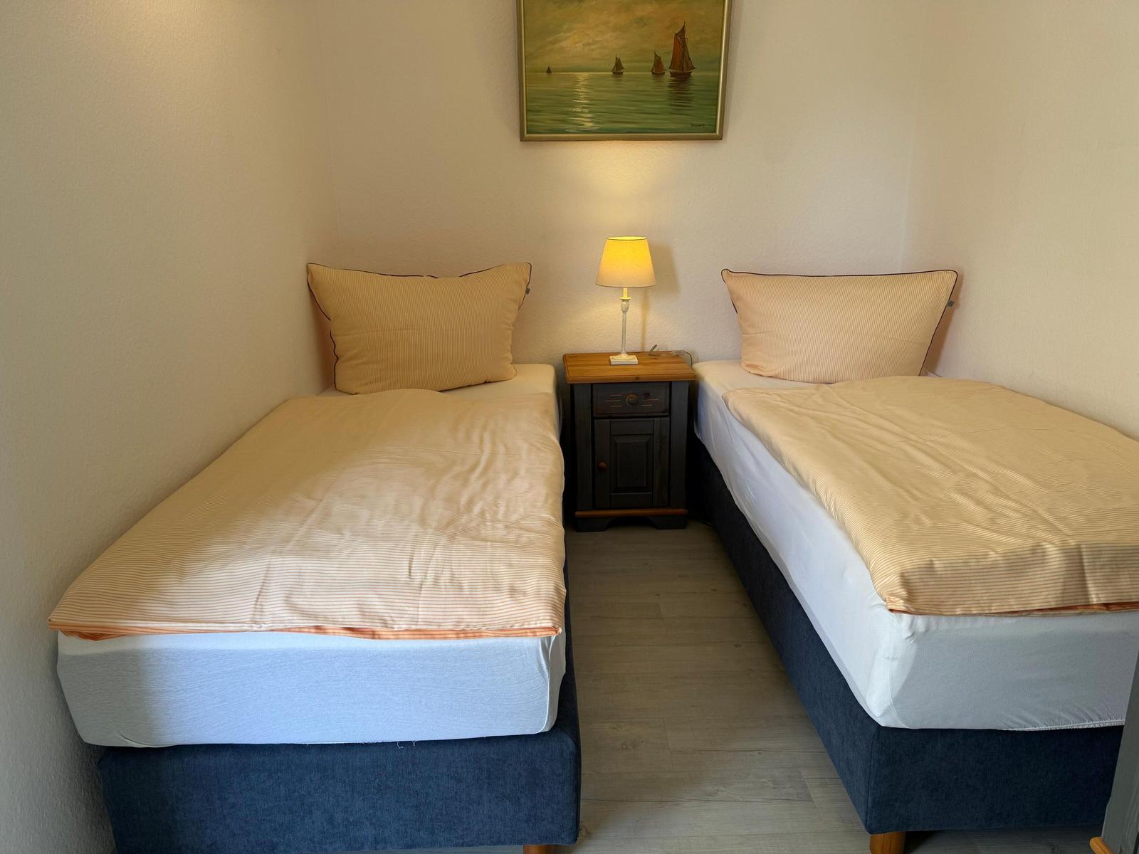 Zwei Einzelbetten mit Bettwäsche, Nachttisch und Wandbild.