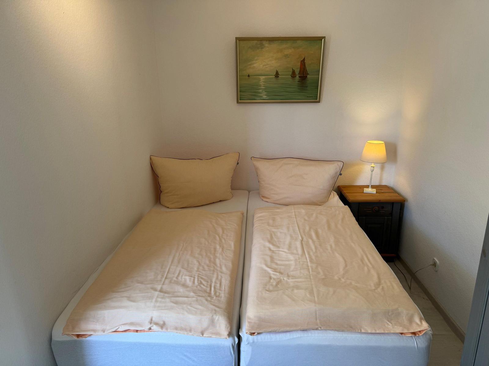 Zwei Einzelbetten mit Bettwäsche, Nachttisch und Lampe. Wandbild mit Segelbooten.