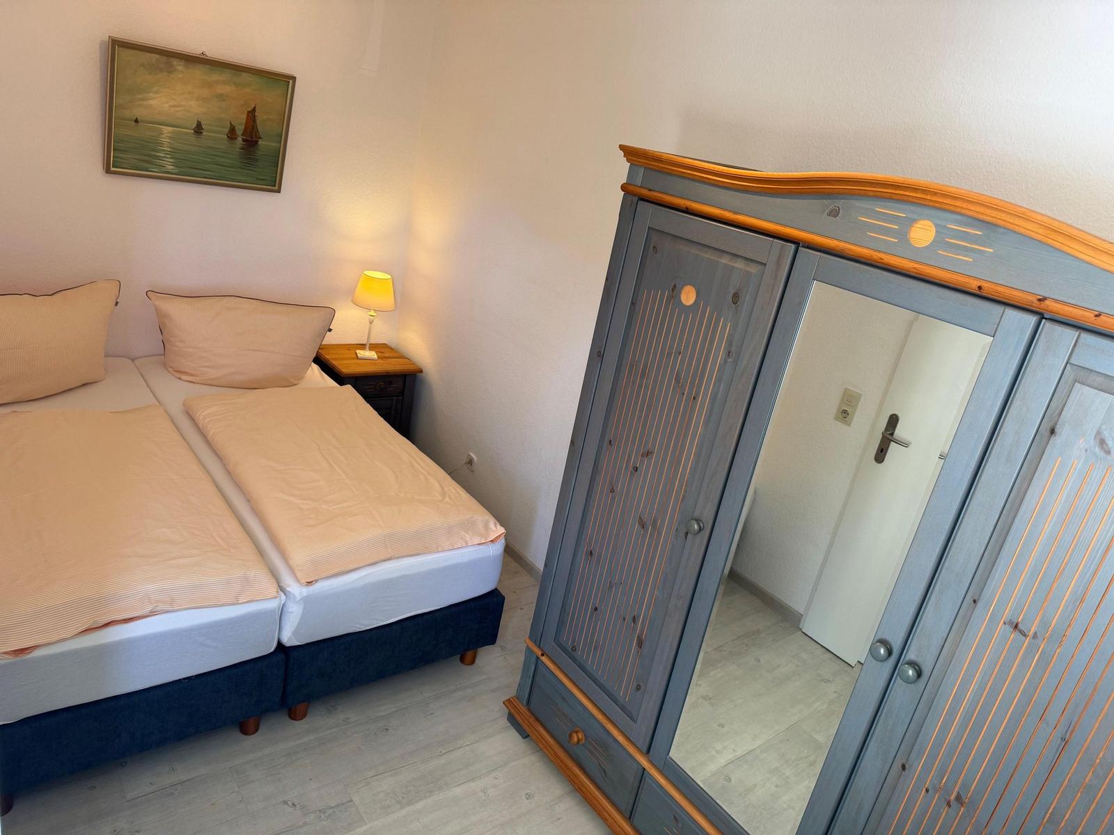 Zimmer mit Doppelbett, Kleiderschrank und Nachttisch mit Lampe.