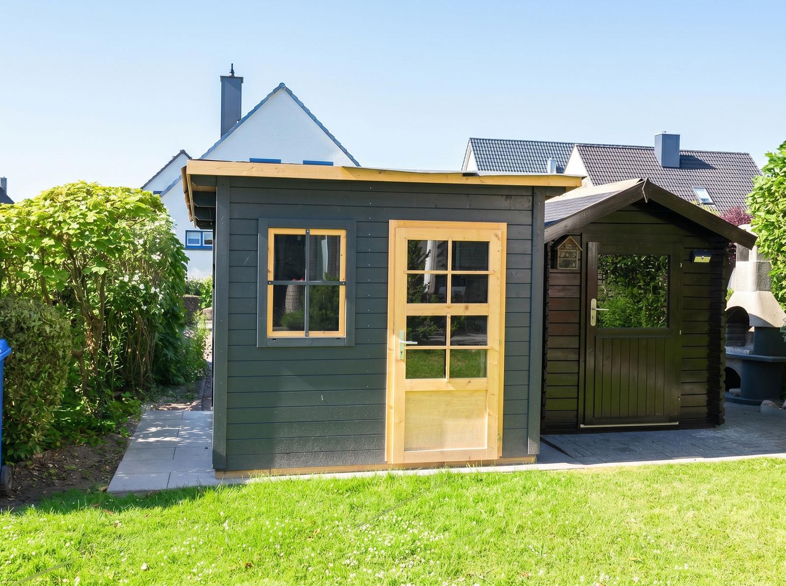 Holzhaus mit Tür und Fenster im Garten. Neben einem kleineren Anbau.
