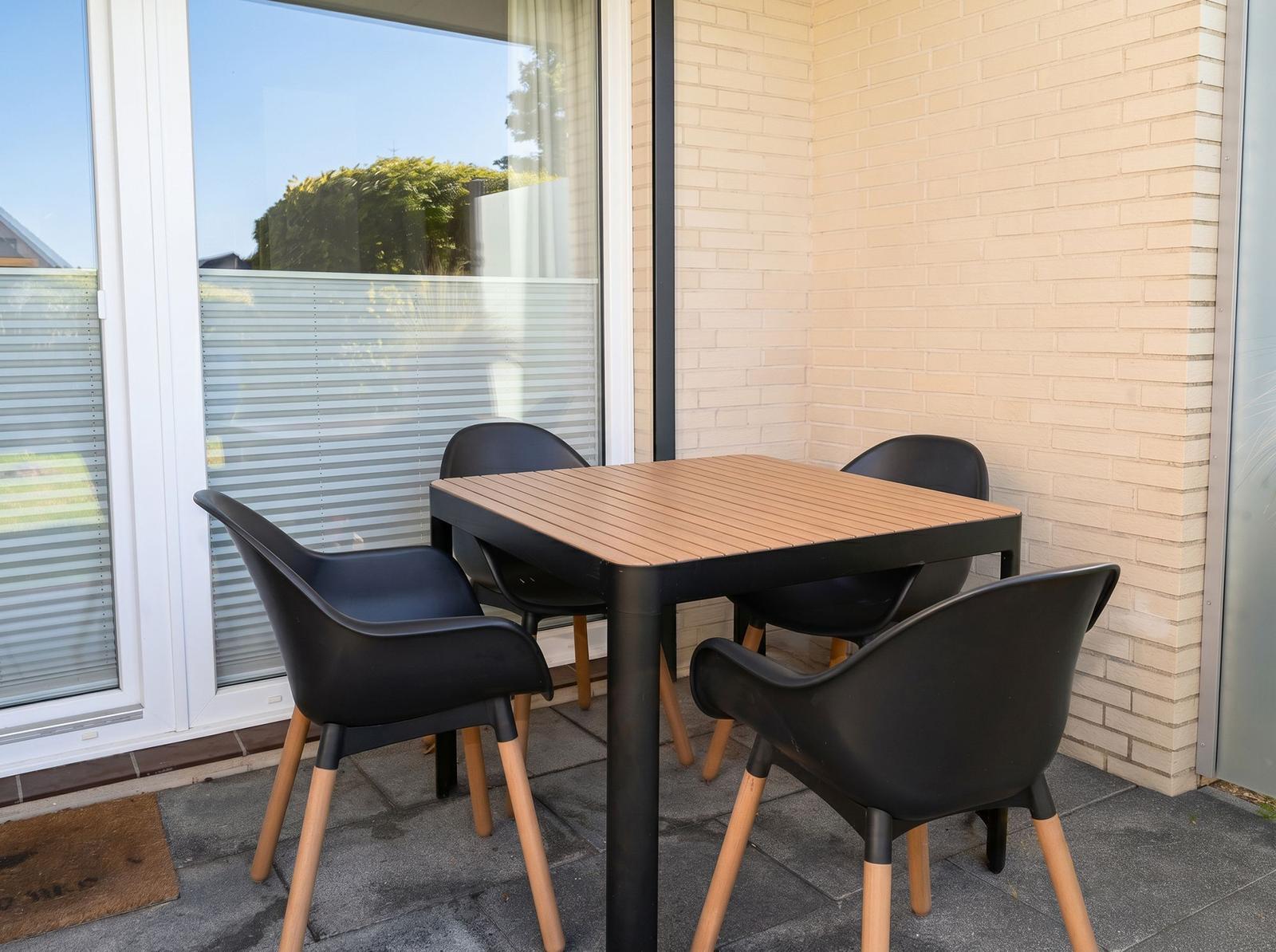 Terrasse mit Tisch und vier Stühlen vor Fenster mit Jalousie.
