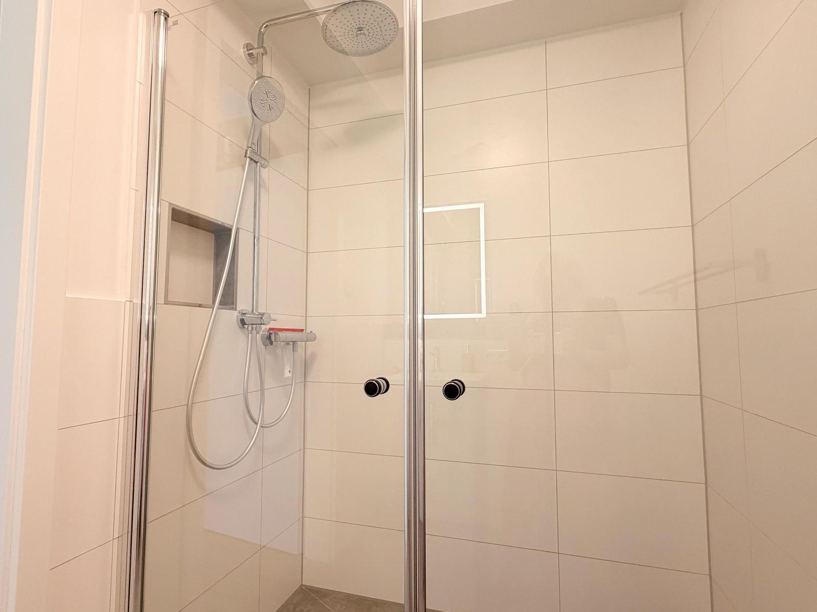 Duschkabine mit Duschbrause und eingelassenem Spiegelfeld an der Wand.