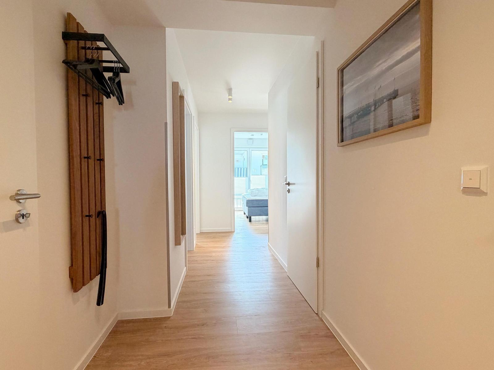 Flur mit Holzboden, Kleiderständer und Wandbild. Blick in Schlafzimmer mit Bett.