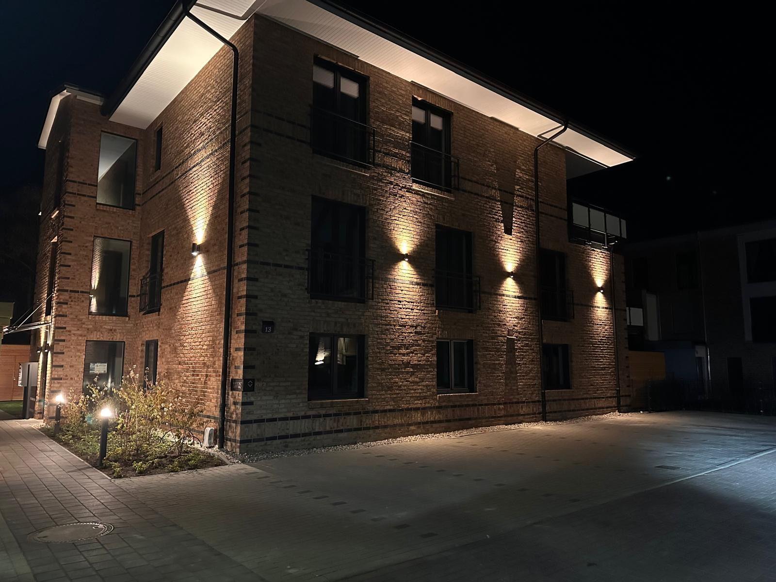 Modernes Backsteinhaus mit Außenbeleuchtung und Balkonen bei Nacht.