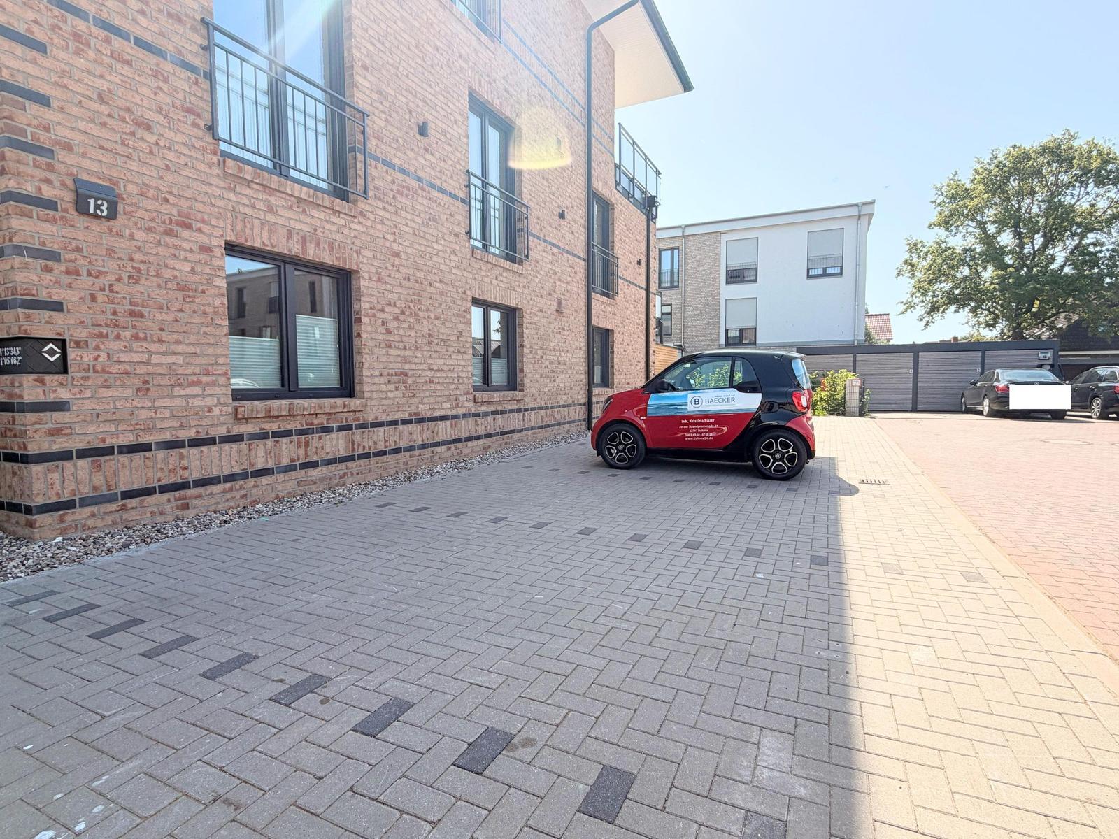Fassade eines modernen Mehrfamilienhauses mit gepflastertem Hof und parkendem Auto.