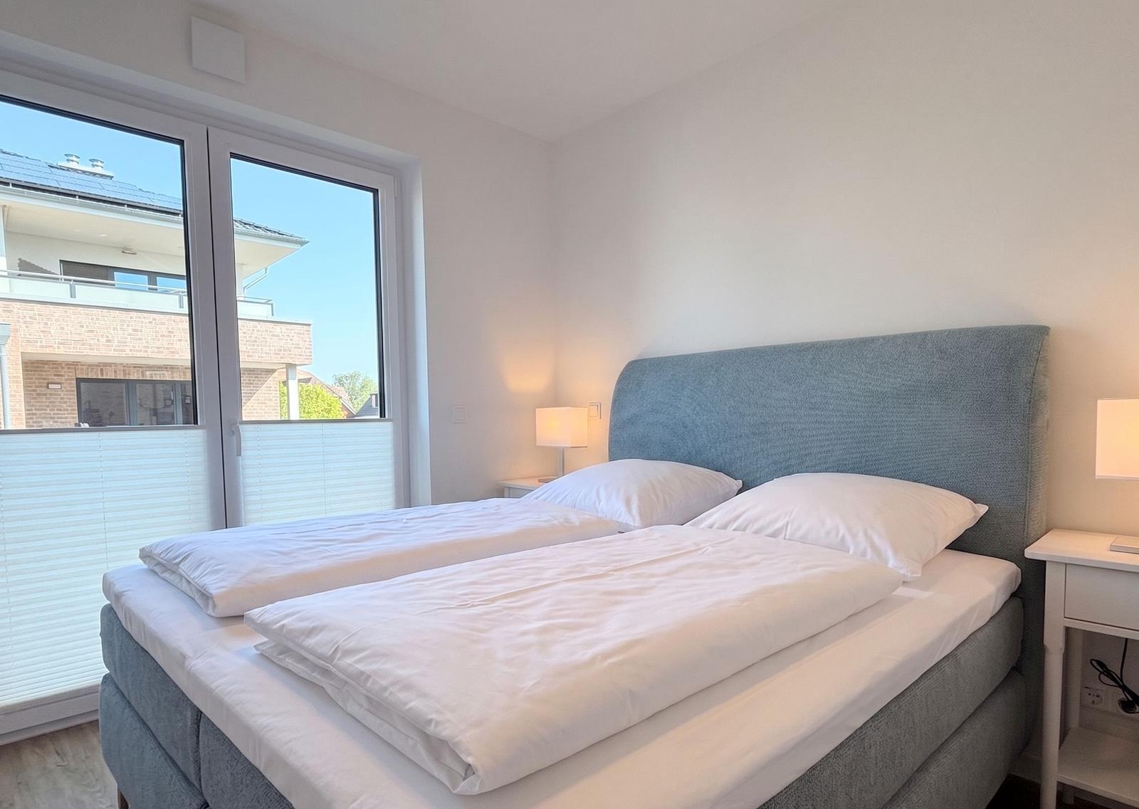 Schlafzimmer mit Doppelbett, Fenster und Nachttischen.