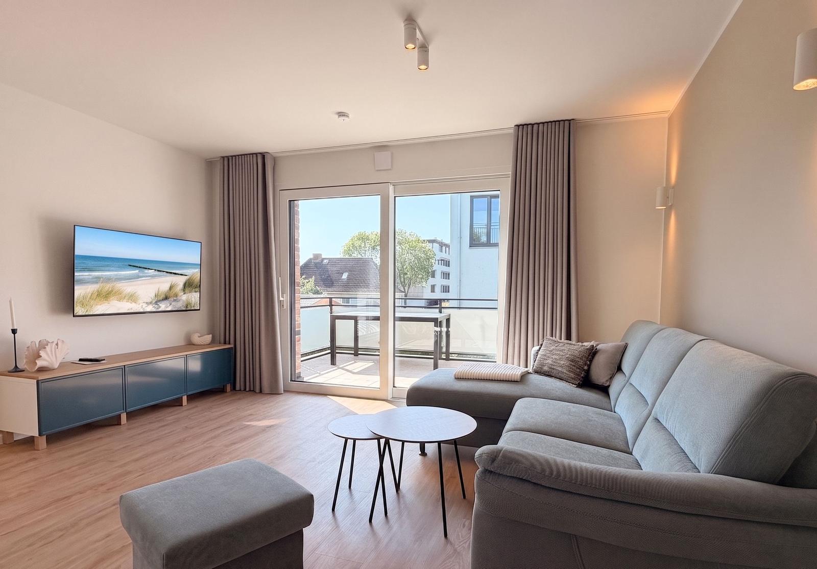 Wohnzimmer mit Sofa, TV und Balkonansicht