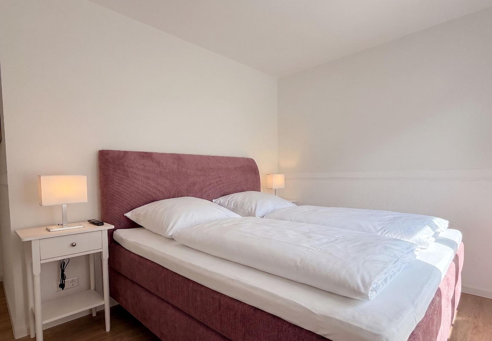 Schlafzimmer mit Bett, zwei Nachttischen und Lampen.