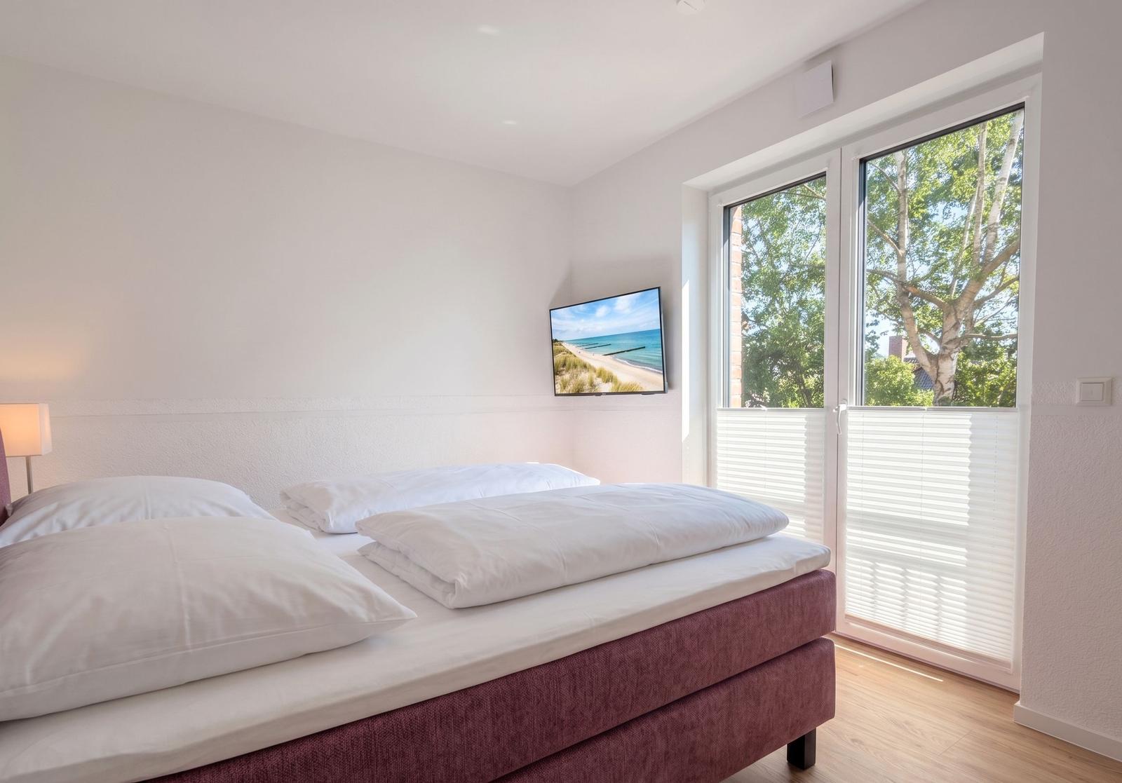 Schlafzimmer mit Bett, TV und Fenster zur Außenseite.