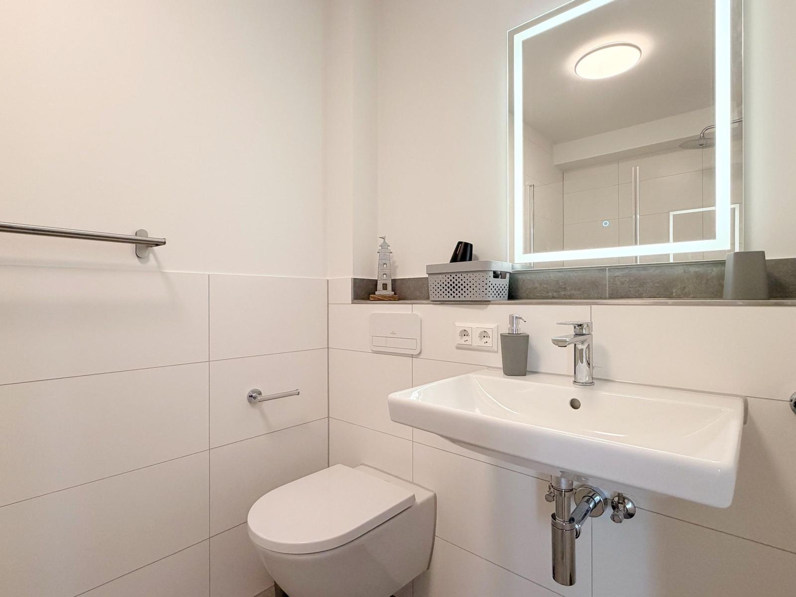 Badezimmer mit Toilette, Waschbecken und beleuchtetem Spiegel