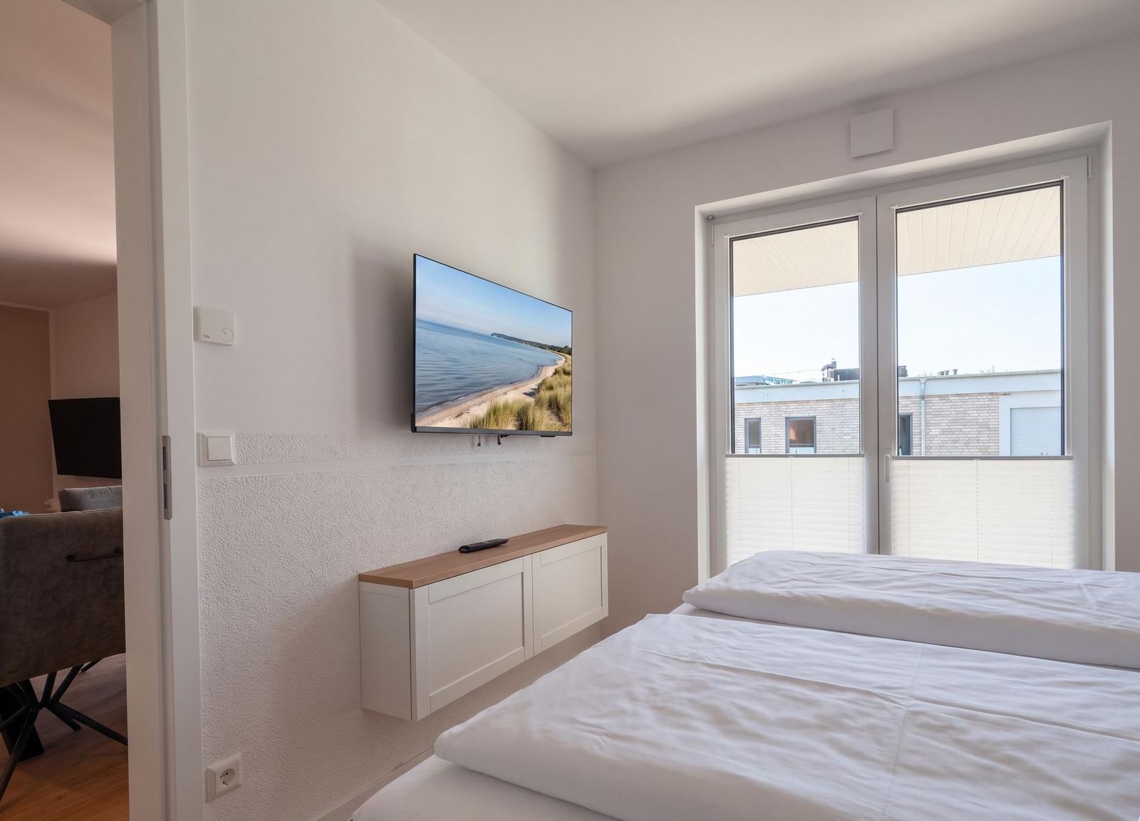 Schlafzimmer mit Doppelbett, TV und Balkonansicht.
