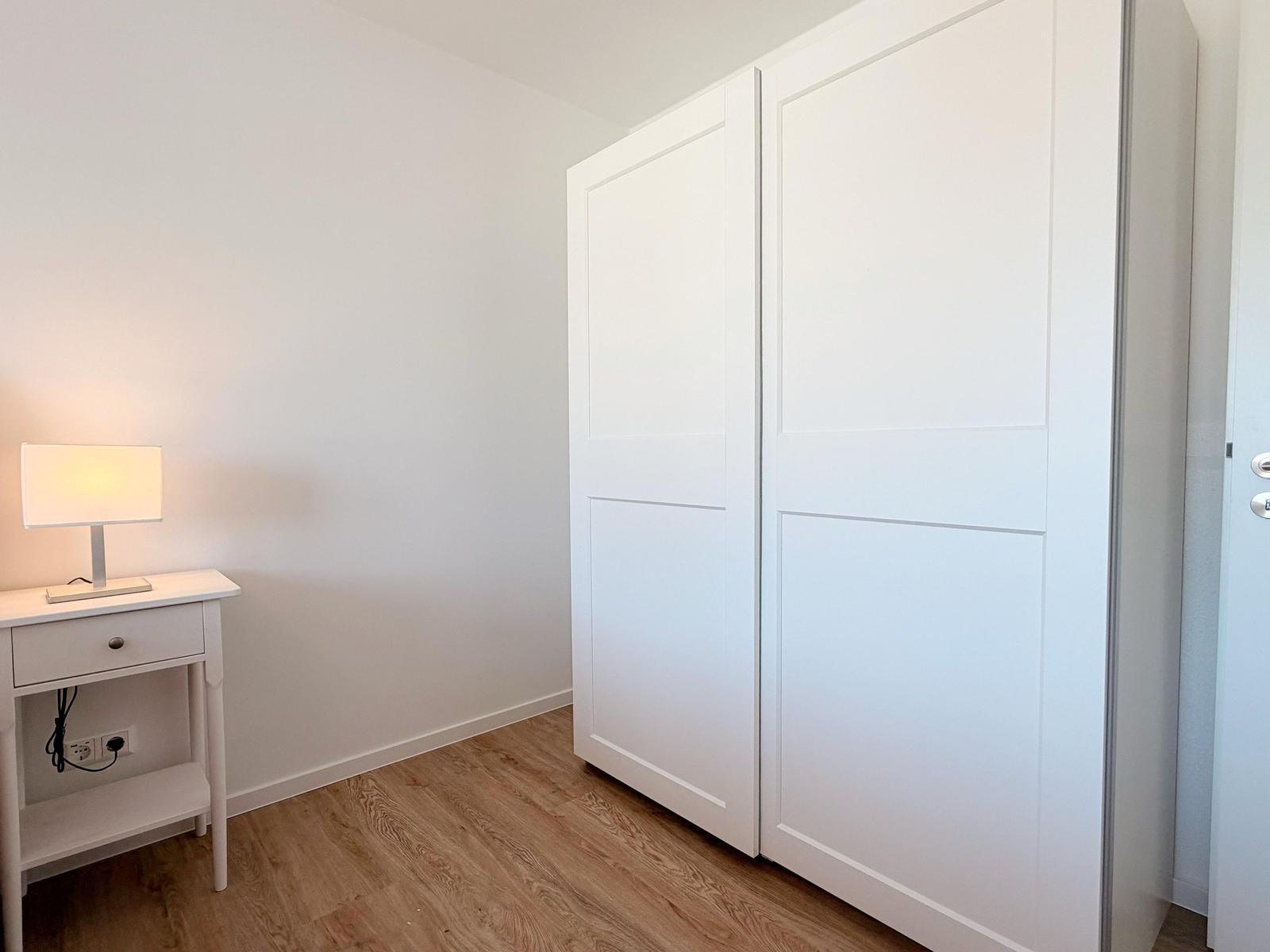 Schlafzimmer mit weißen Schiebetüren und Nachttisch mit Lampe.