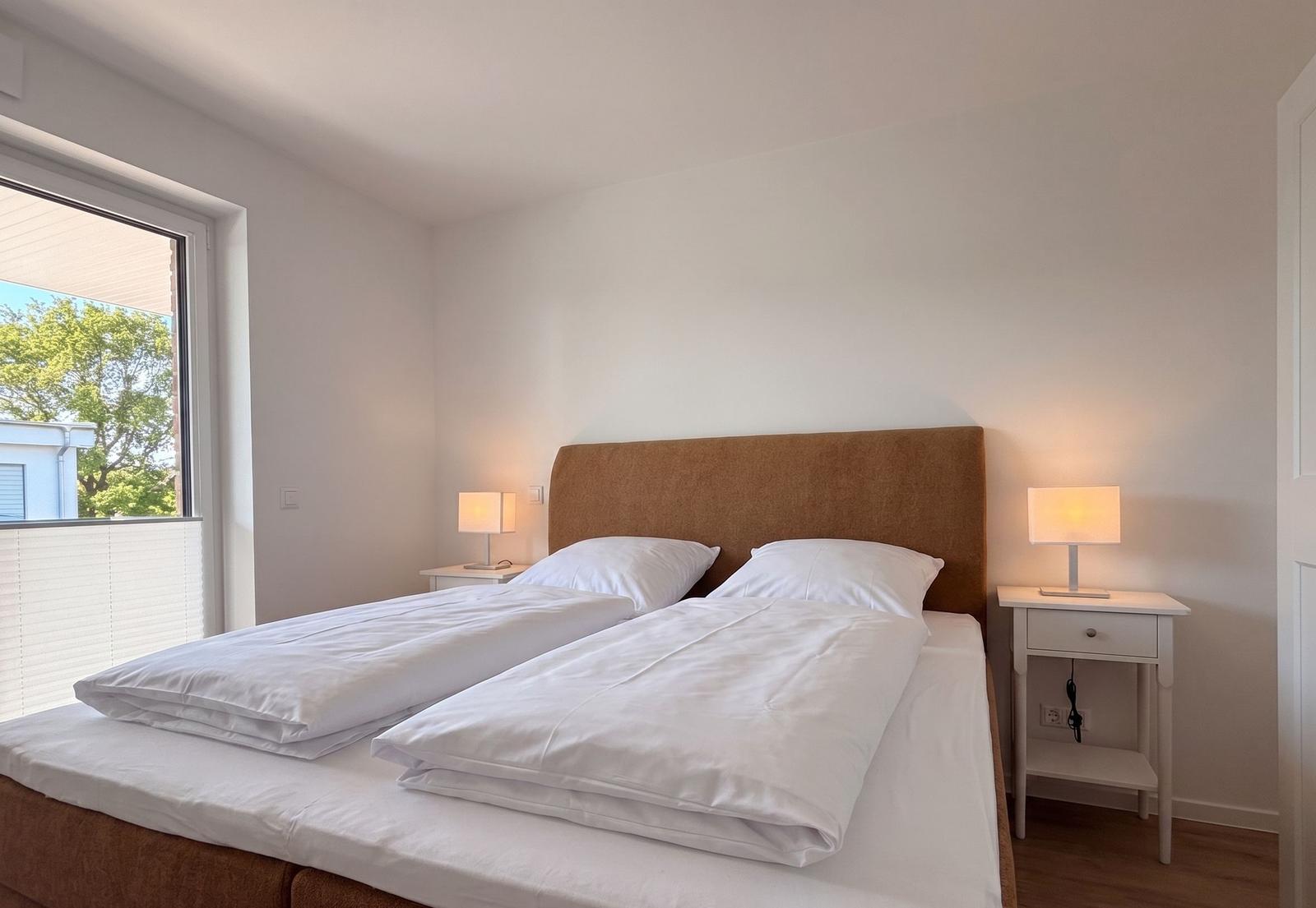 Schlafzimmer mit Doppelbett, zwei Nachttischen und Lampe. Fenster mit Blick auf Außenbereich.
