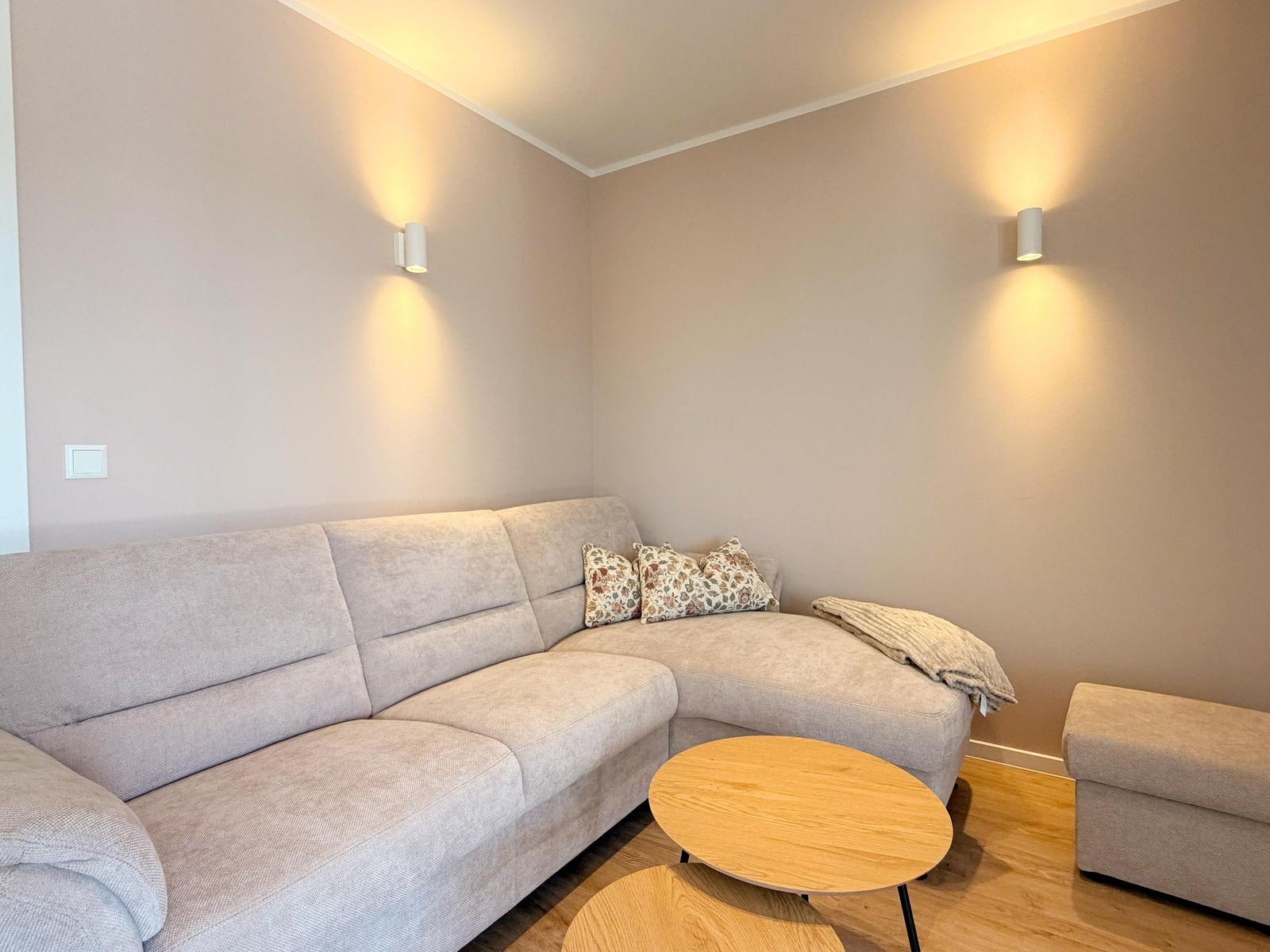Ein Wohnzimmer mit Ecksofa, Holztisch und Wandlampen.