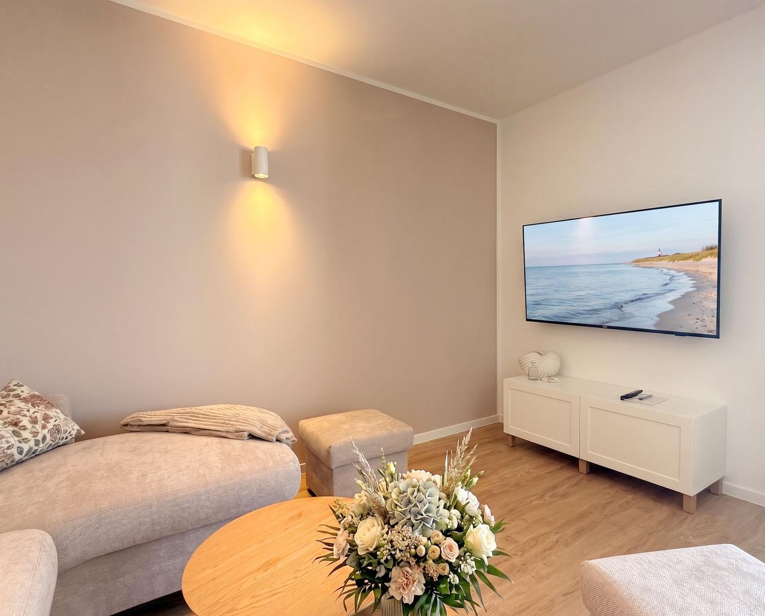 Wohnzimmer mit Sofa, Fernseher und Blumenvase auf Tisch.
