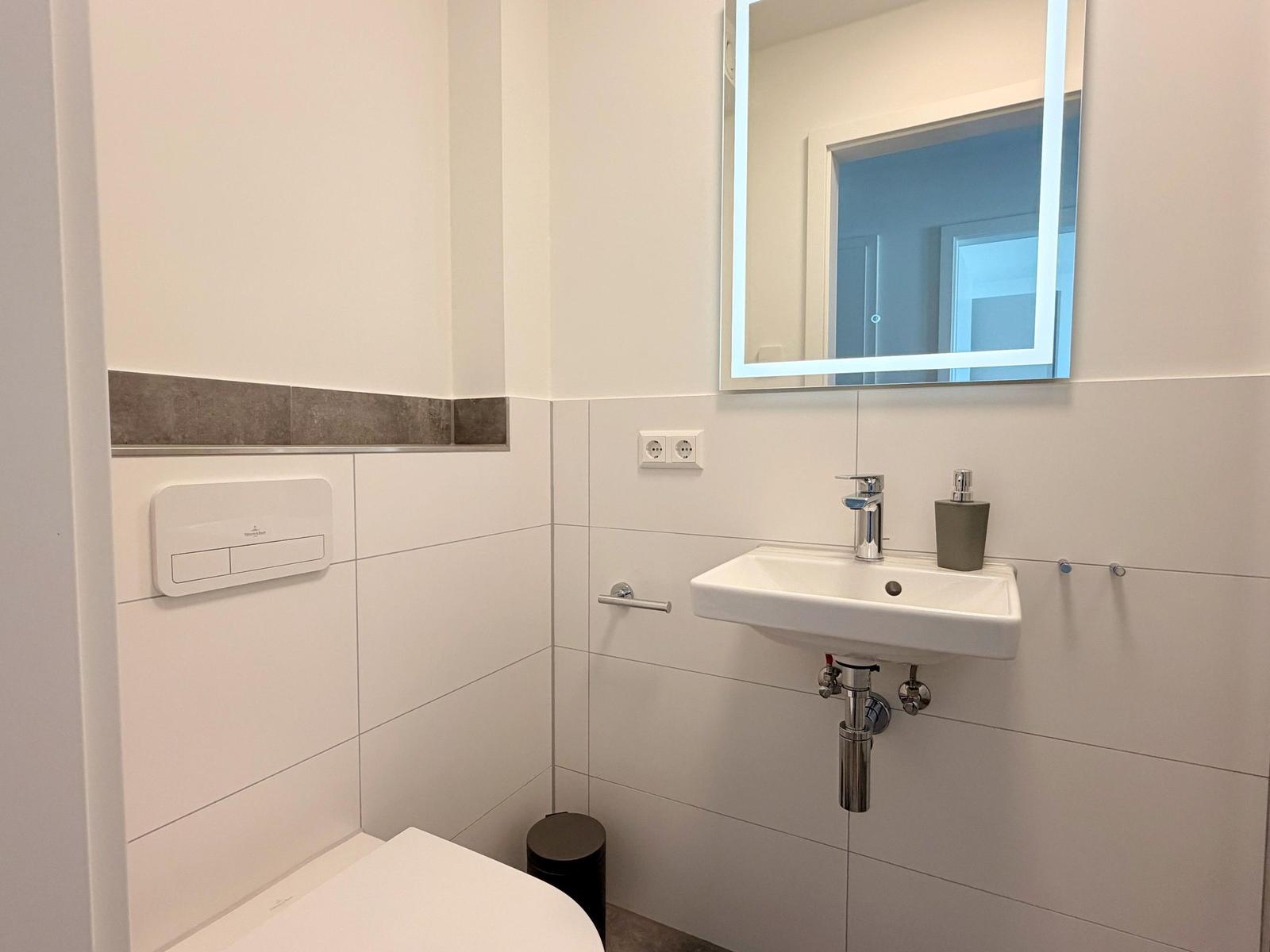 Badezimmer mit Waschbecken, Spiegel und Toilette. Wandfliesen und moderne Armaturen.