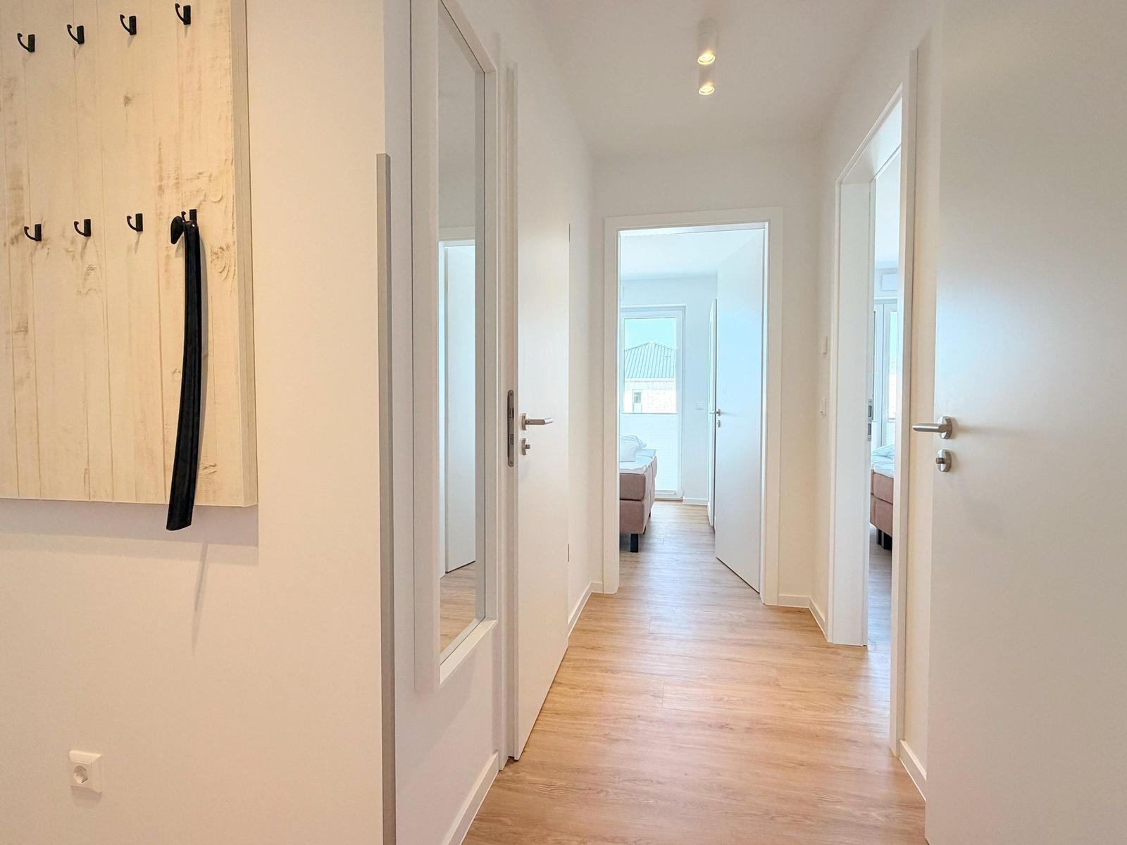 Flur mit Holzboden, Spiegeltüren und Garderobe mit Haken.