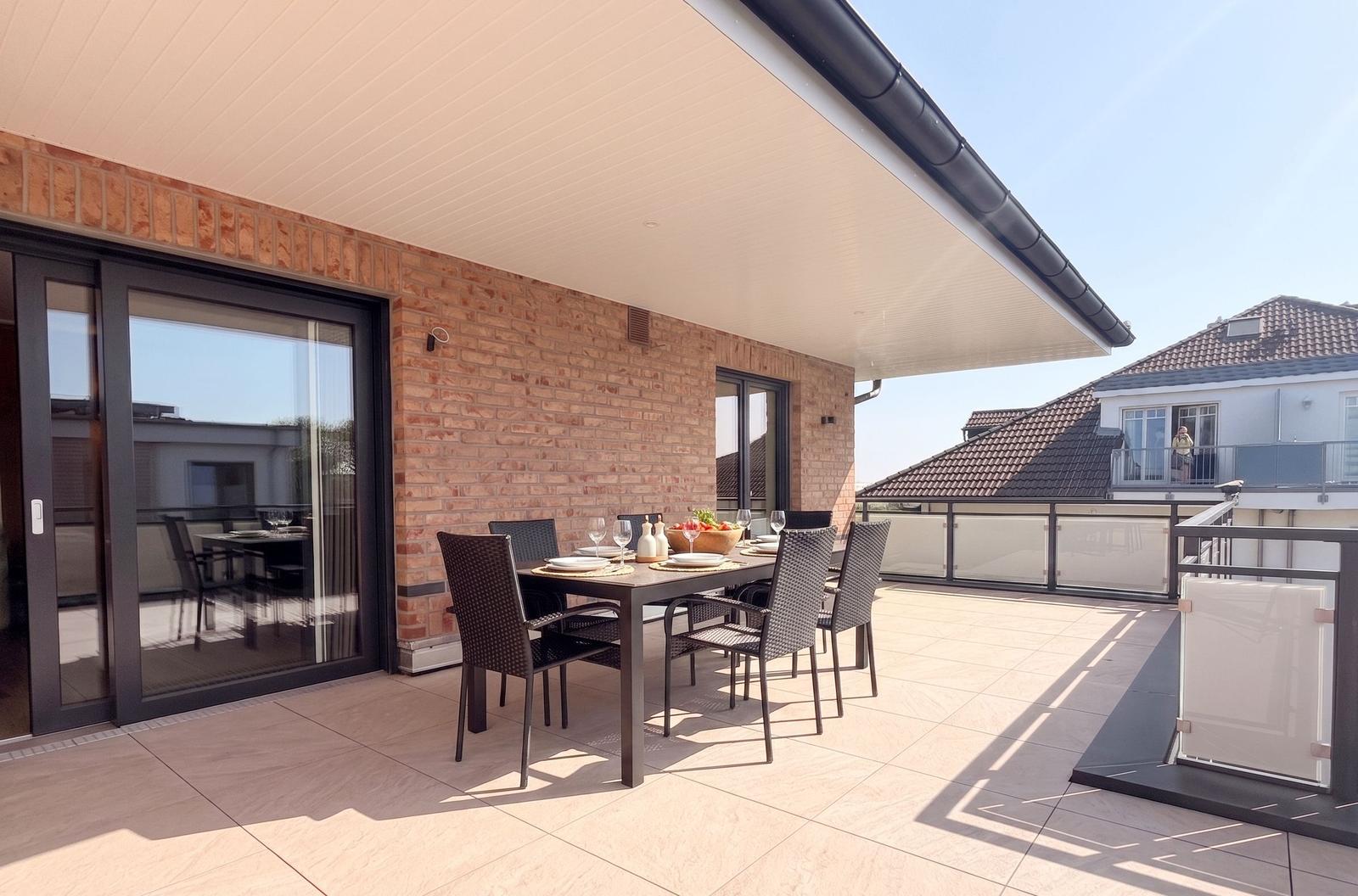 Terrasse mit Tisch und Stühlen, glasverkleidete Balkontüren und Sicht auf benachbarte Häuser.