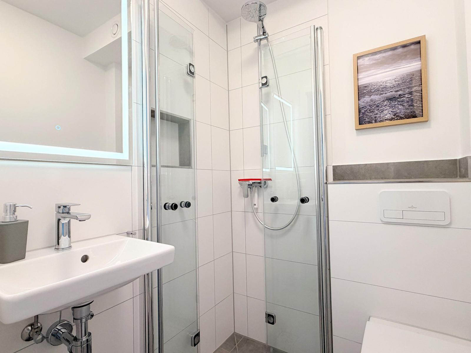 Badezimmer mit Dusche, Waschbecken und Spiegel.