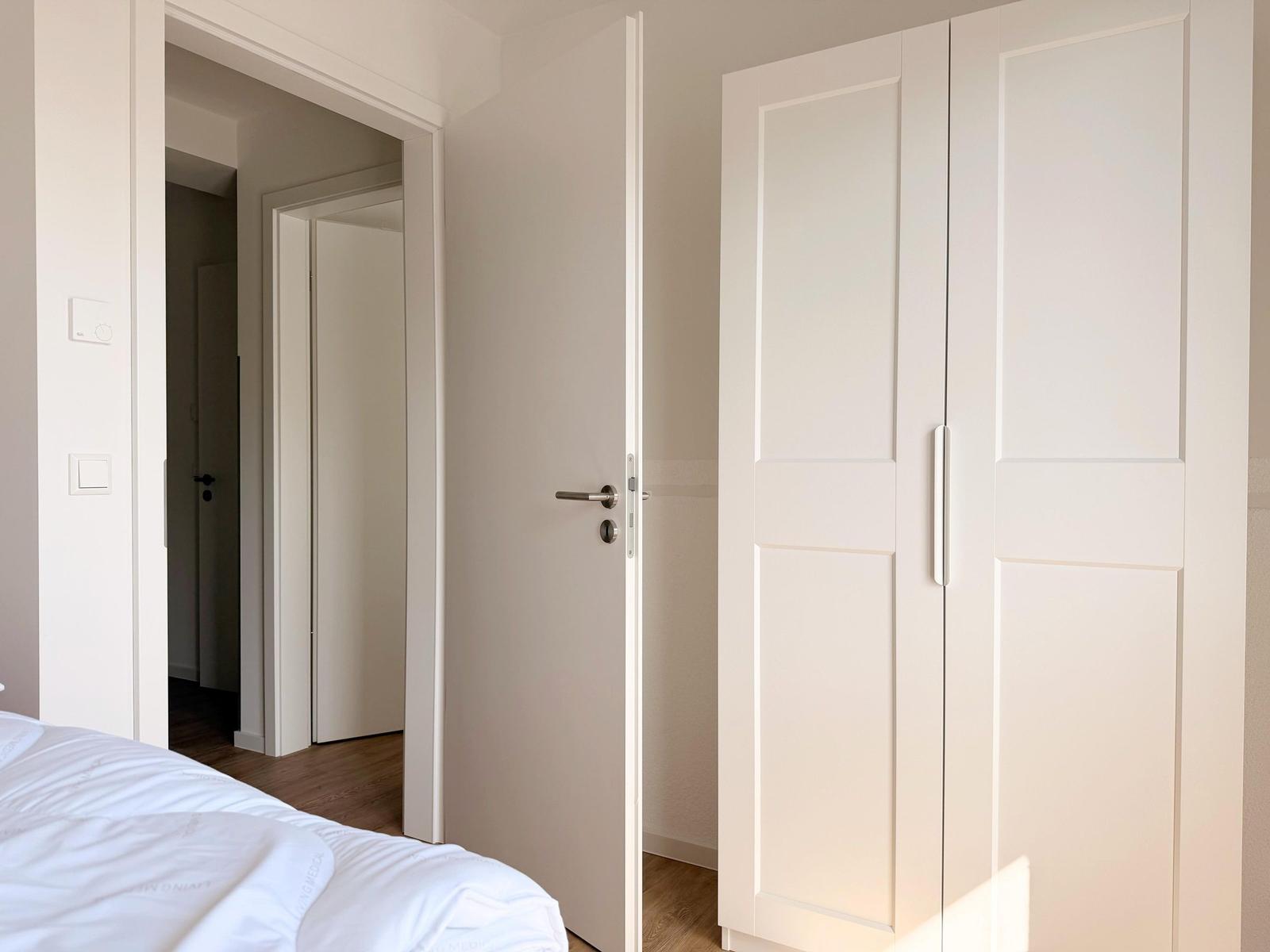 Schlafzimmer mit weißem Kleiderschrank und Tür. Bett und Holzboden sind sichtbar.