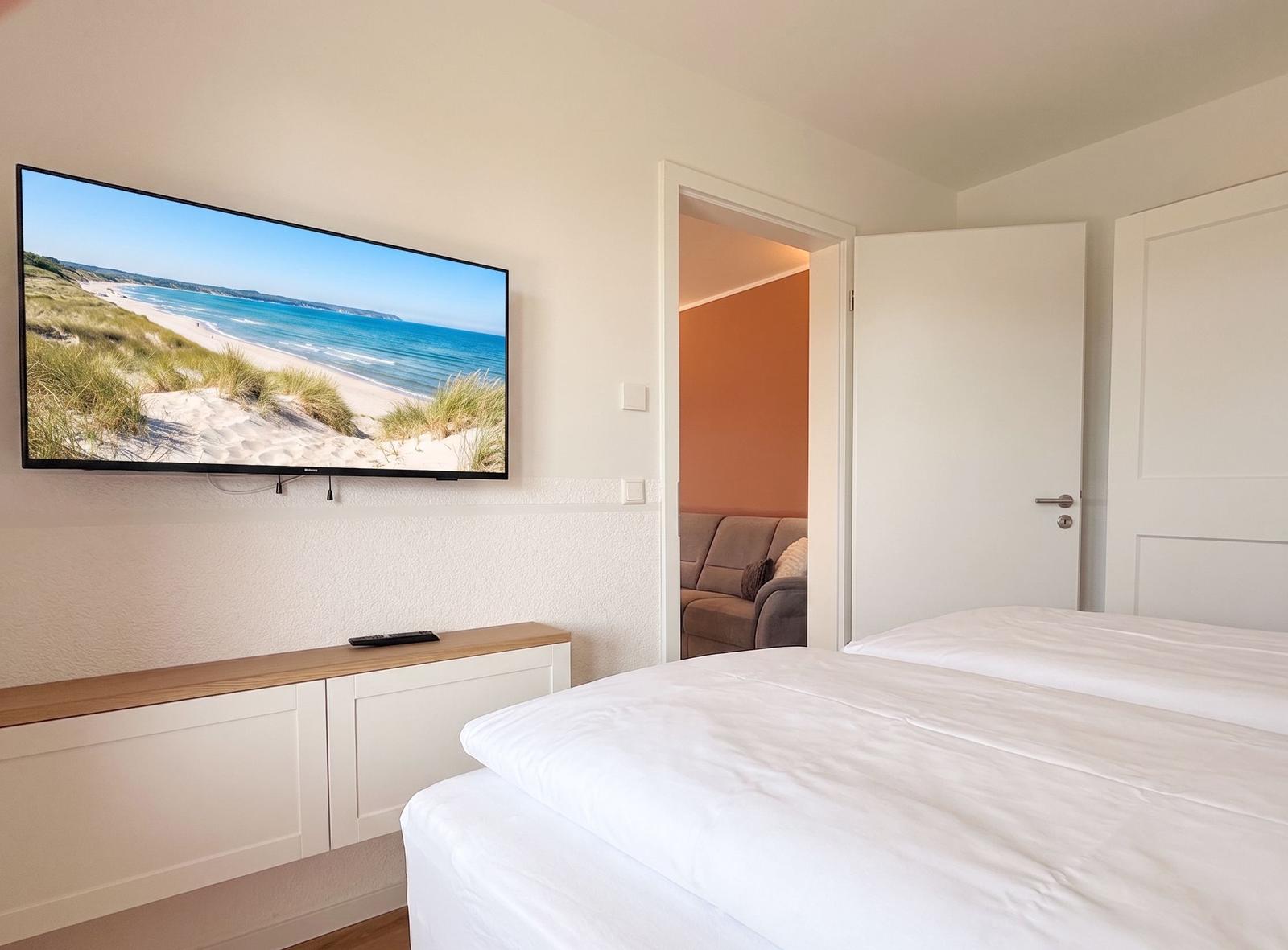 Schlafzimmer mit Bett, Fernseher und Blick in Wohnbereich.