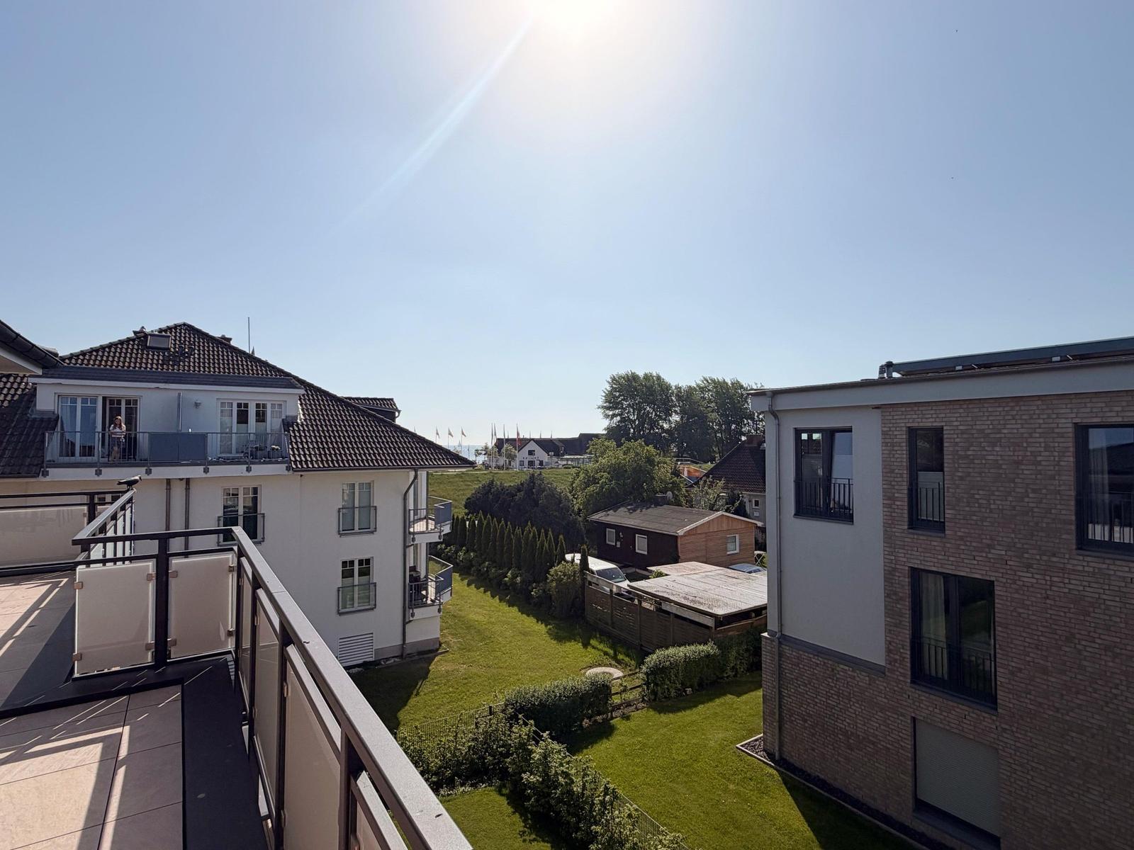 Terrasse mit Blick auf Wohnhäuser und Grünfläche unter blauem Himmel.