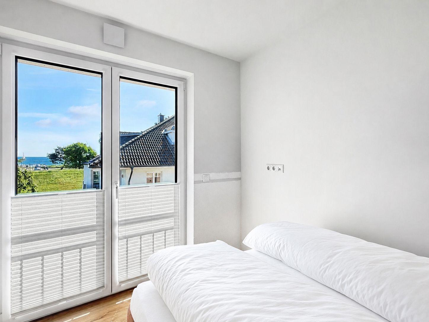 Schlafzimmer mit Blick auf Meer und Grünfläche durch Glastür.