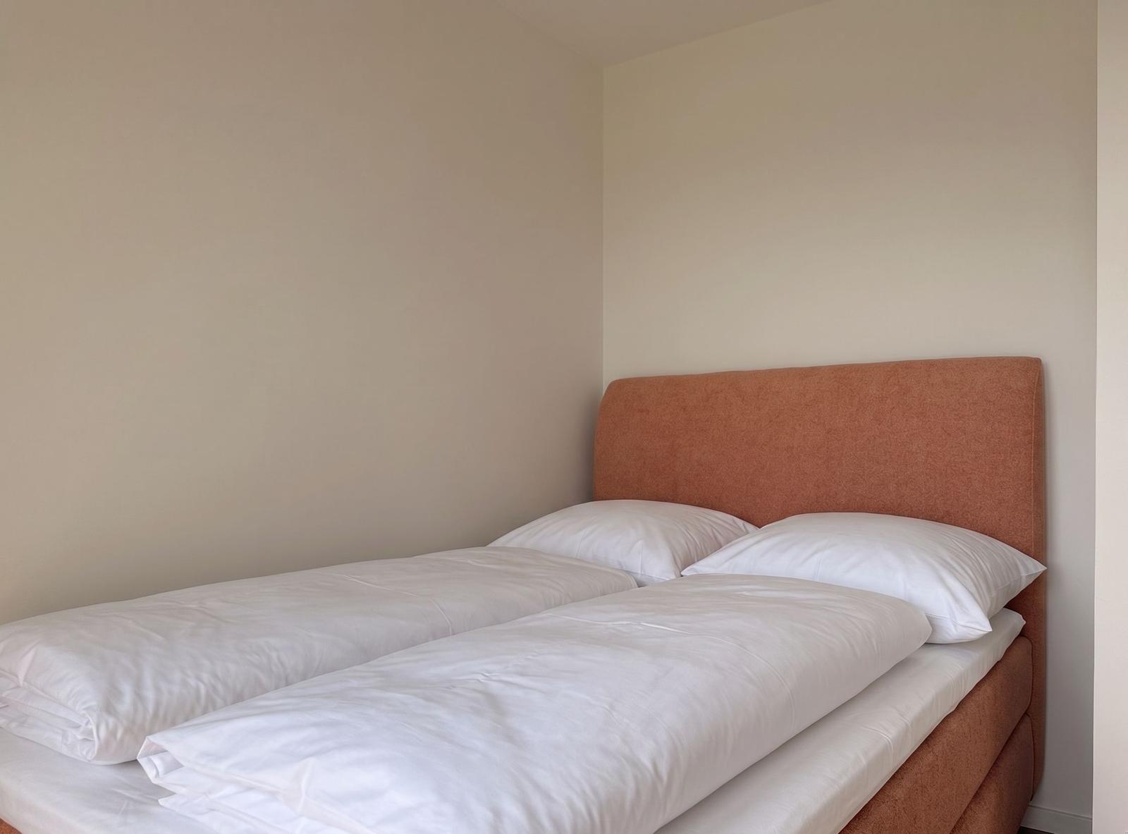 Schlafzimmer mit Doppelbett und orangefarbenem Kopfteil.