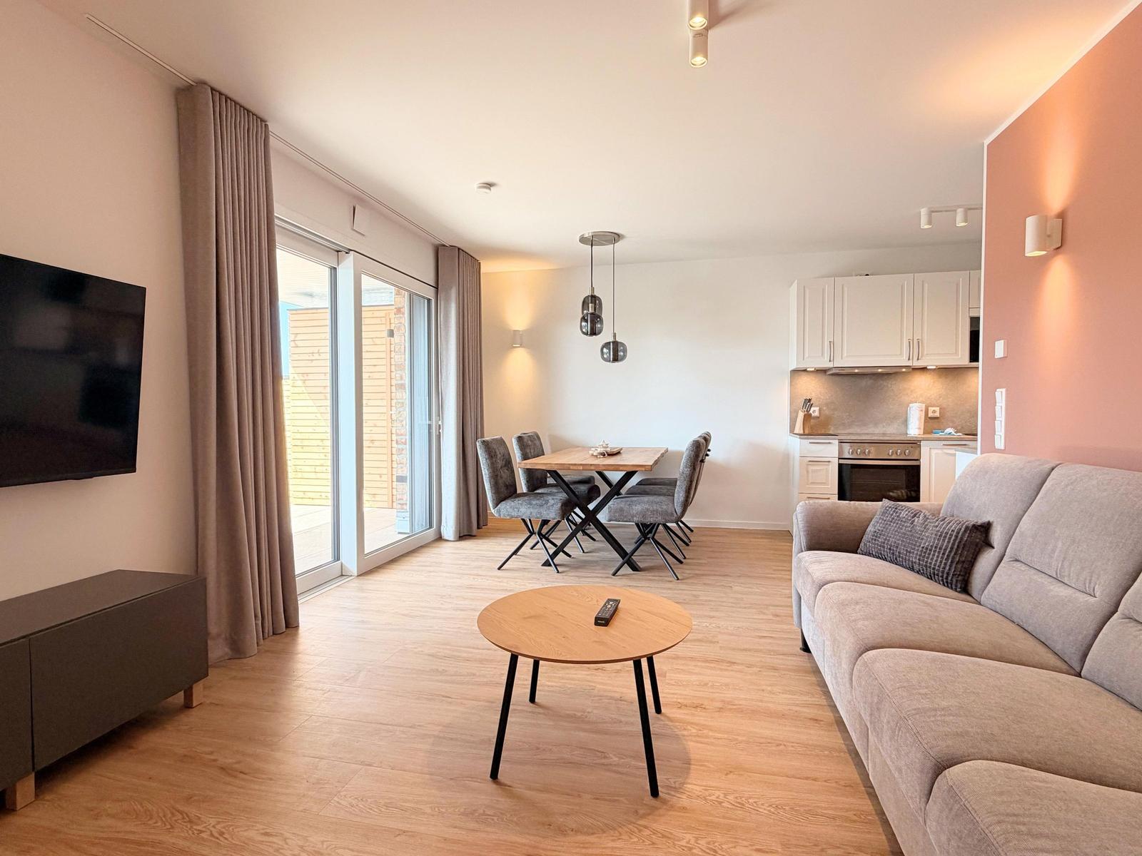 Wohn- und Essbereich mit Sofa, Esstisch und Küche im Hintergrund.